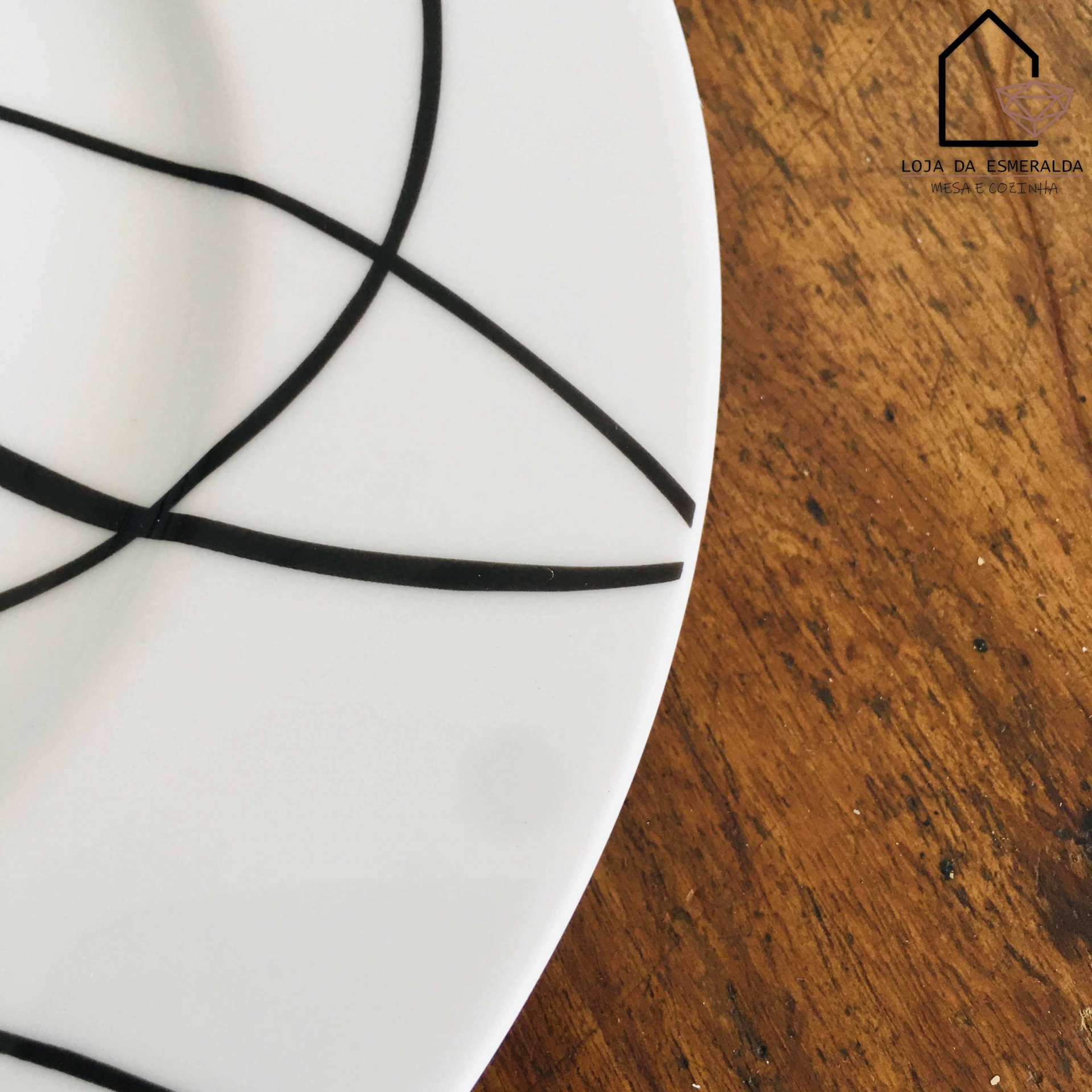 Prato branco com linhas pretas sobre mesa de madeira, logotipo Loja da Esmeralda no canto