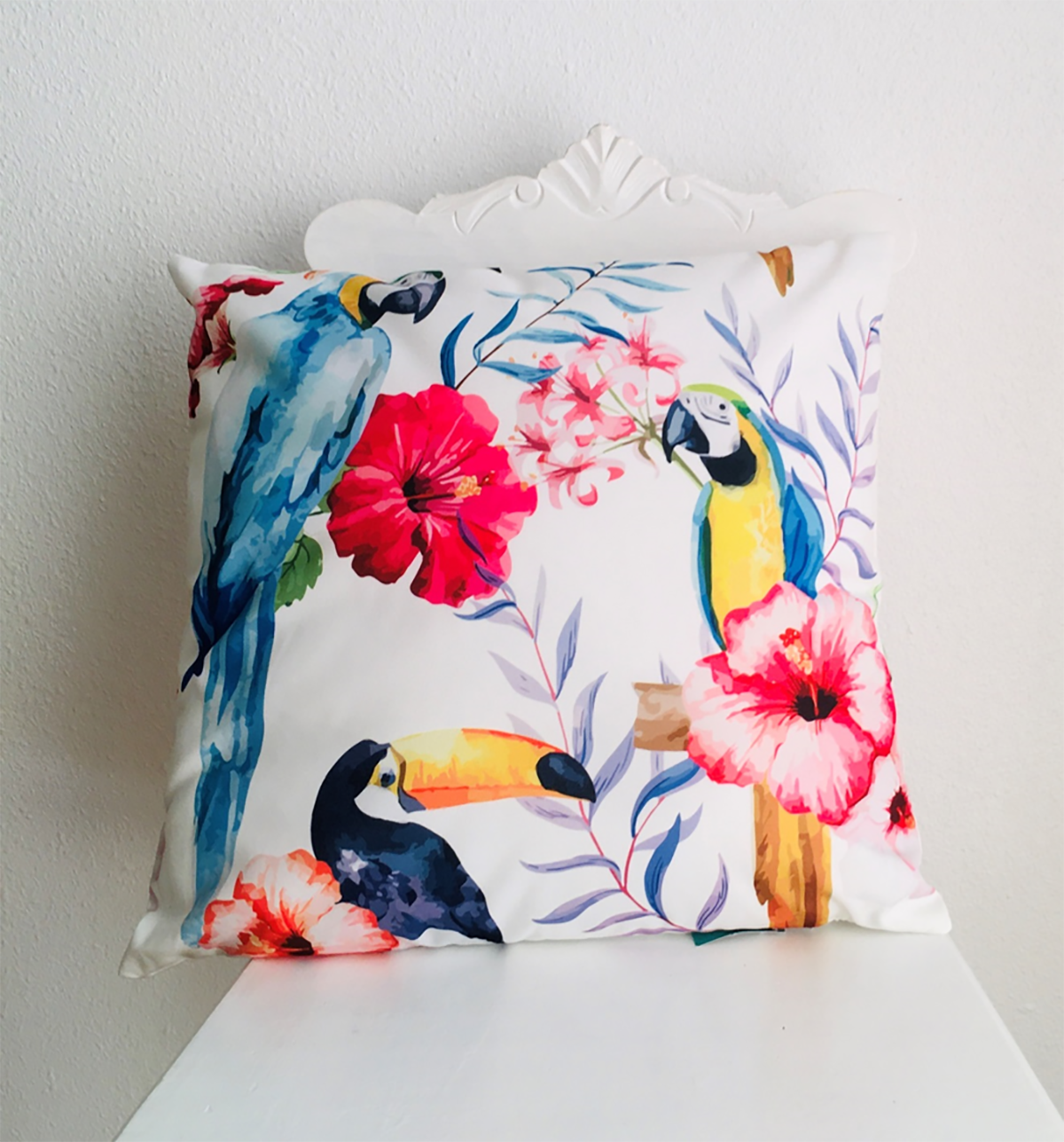 Almofada branca com estampa de papagaios e flores tropicais coloridas