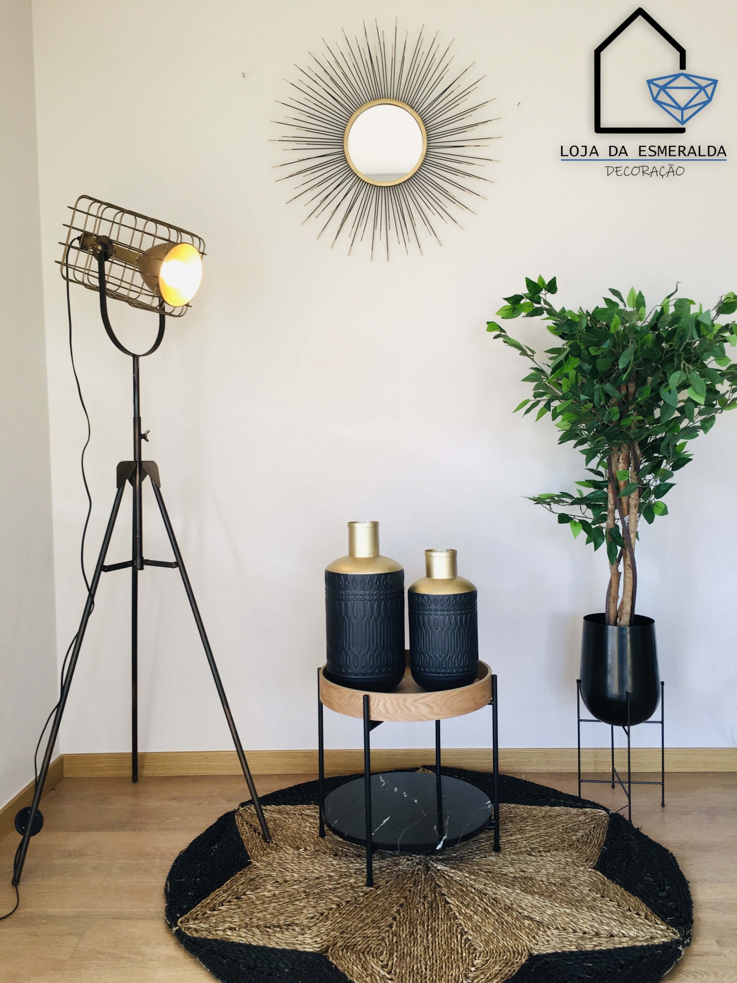 Decoração interior com candeeiro de pé preto, espelho redondo com moldura metálica, vasos pretos com tampa dourada, planta verde em vaso preto e tapete redondo de palha