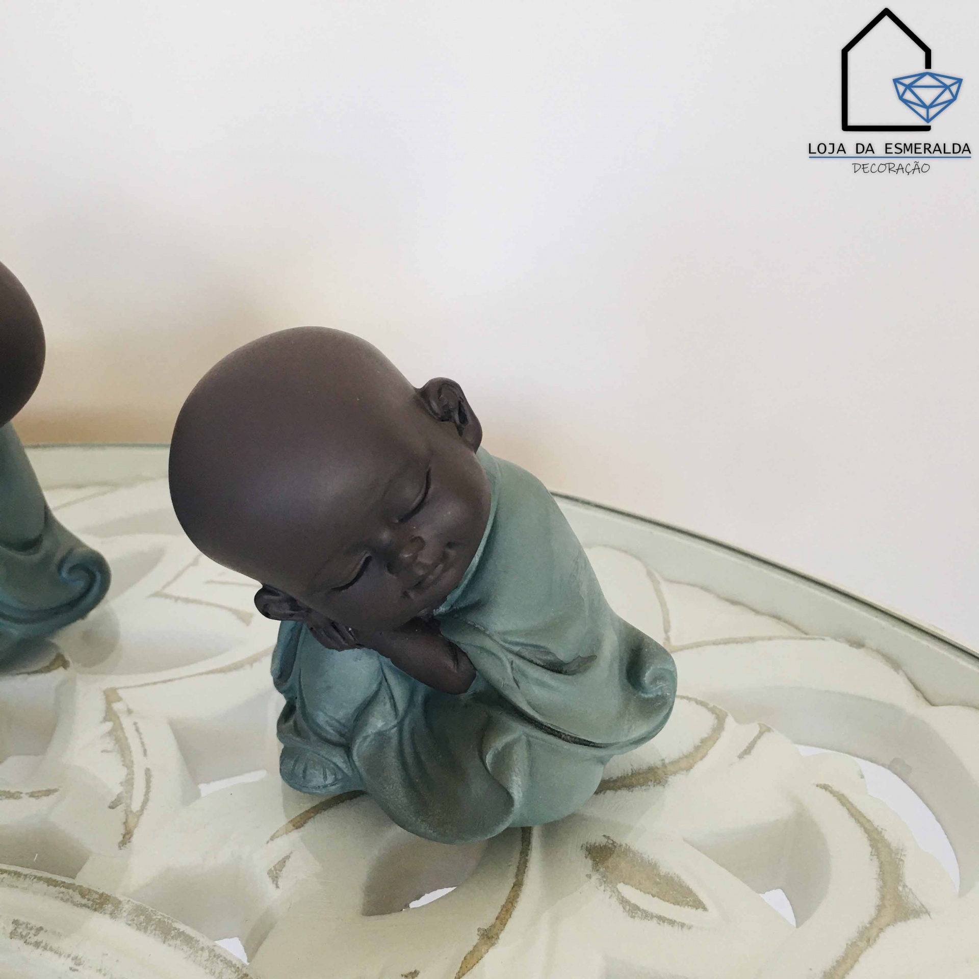 Estatueta de figura sentada com roupa verde água e cabeça castanha em superfície branca com padrão de folhas