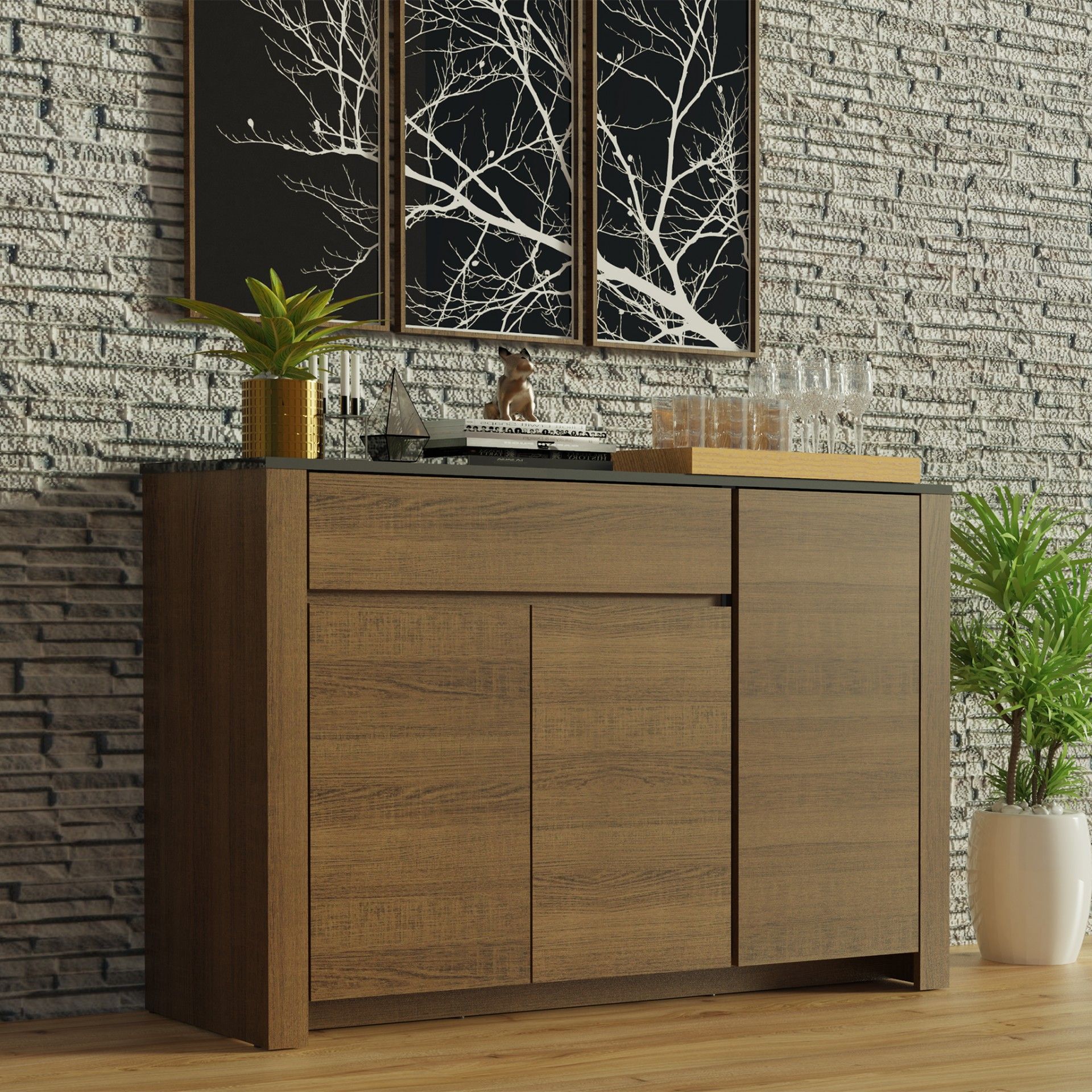 Aparador em madeira castanha com três portas, gaveta e tampo preto, parede de pedra cinzenta e quadros de ramos brancos