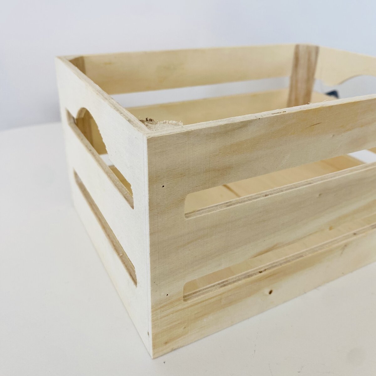 Caixa de madeira clara com recortes laterais e pega
