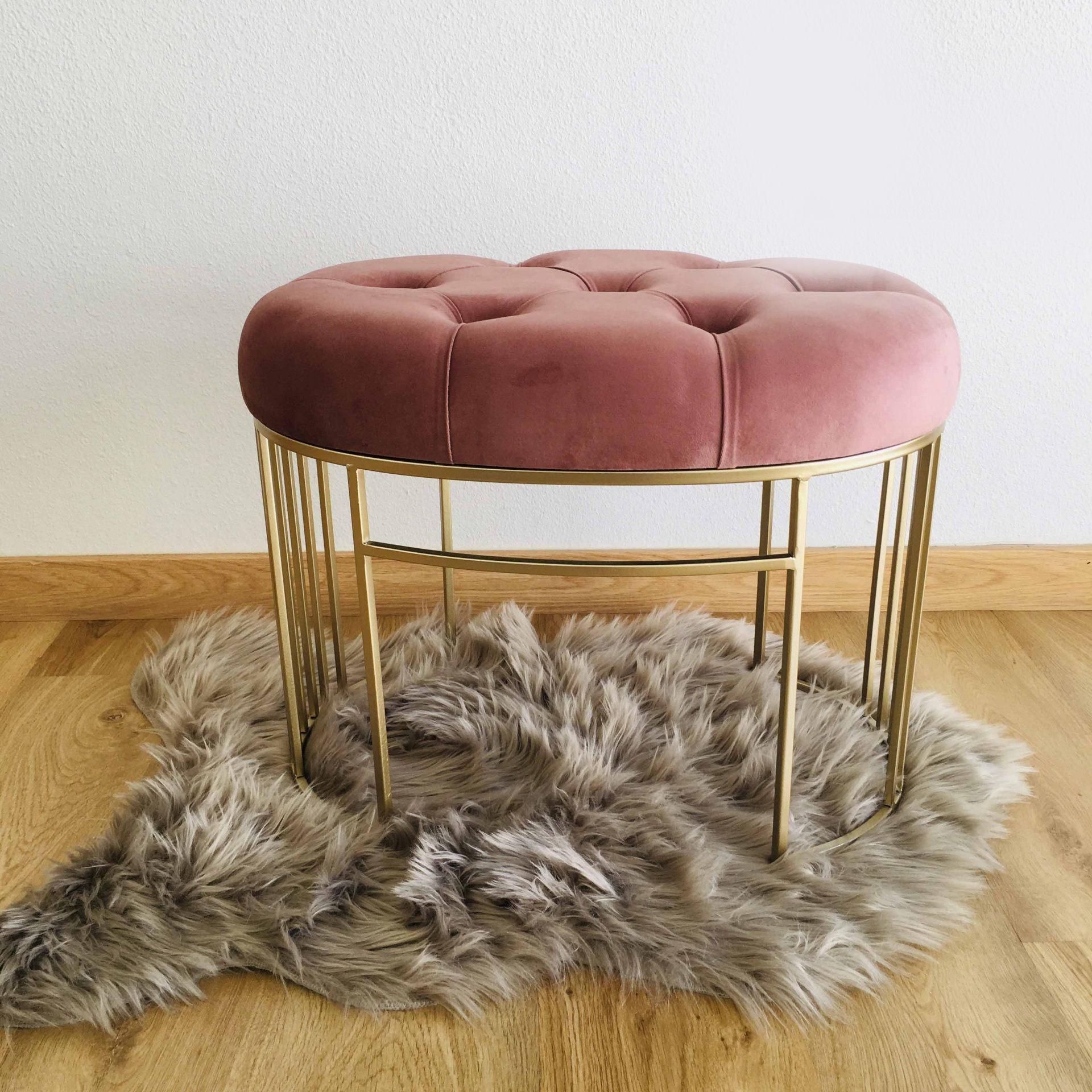 Banco redondo com assento rosa em veludo e estrutura metálica dourada sobre tapete cinza