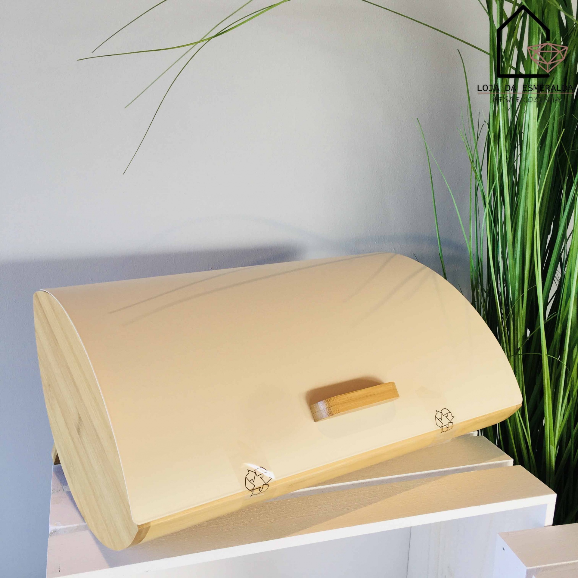 Caixa de pão em madeira clara com puxador em madeira numa superfície branca junto a plantas
