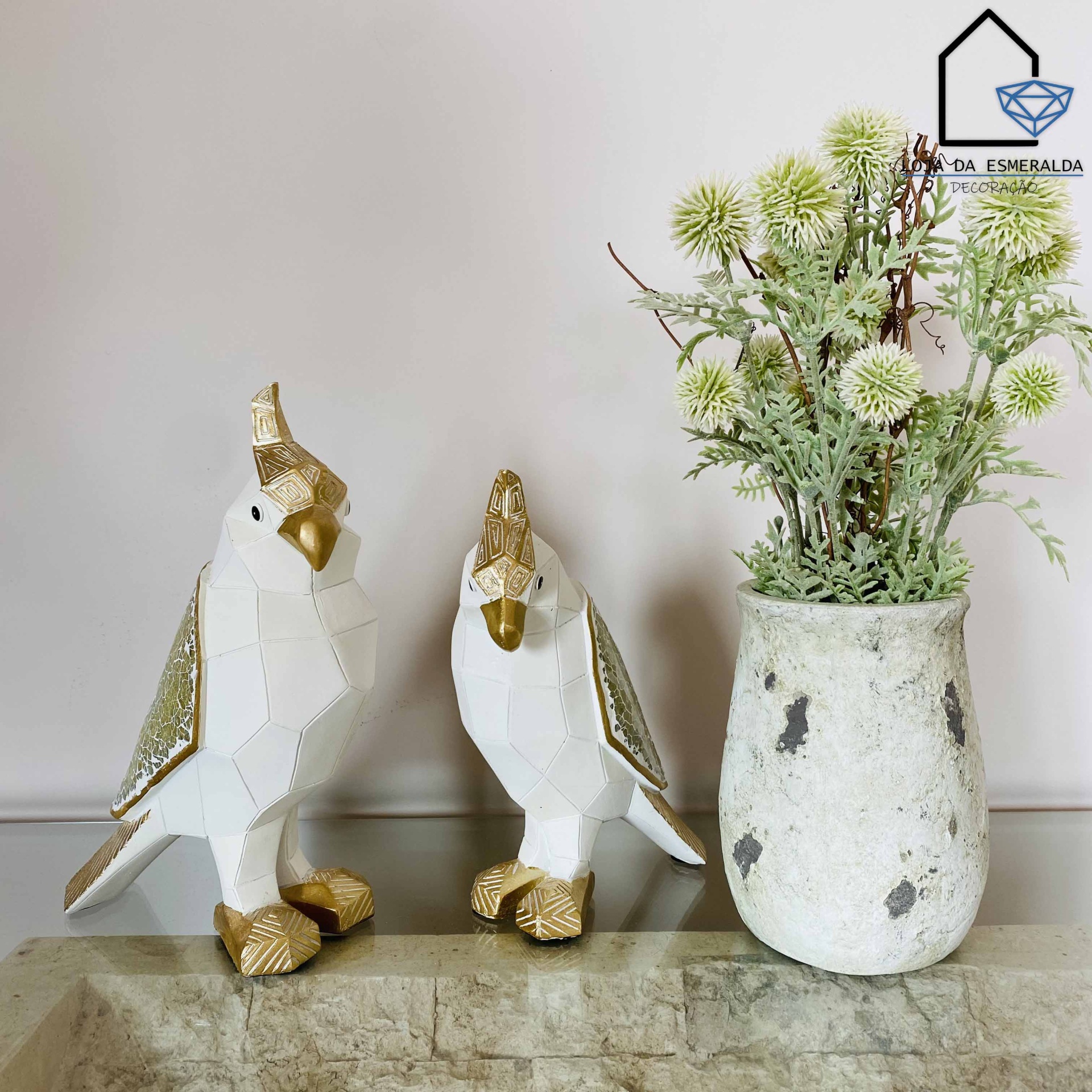 Estátuas de aves brancas e douradas ao lado de um vaso com flores artificiais verdes