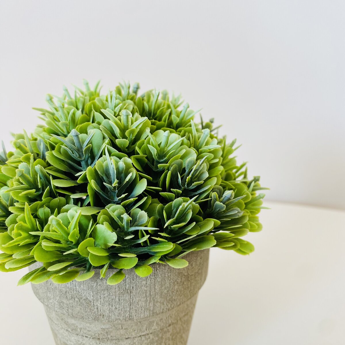 Planta artificial verde num vaso cinza sobre uma superfície branca
