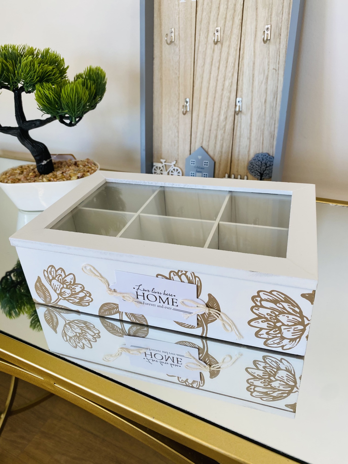 Caixa organizadora branca com tampa de vidro e divisórias, decoração de flores douradas e etiqueta decorativa.