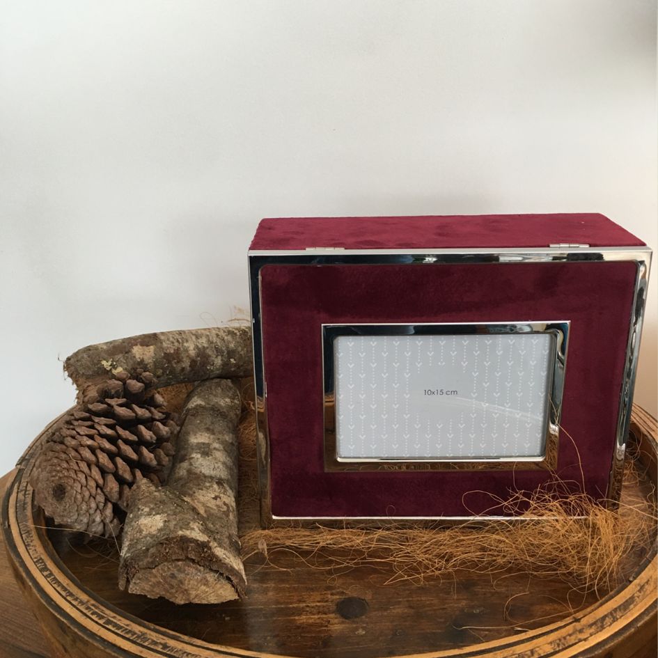 Moldura de fotografia retangular em veludo vermelho com bordas metálicas prateadas e elementos naturais ao lado.
