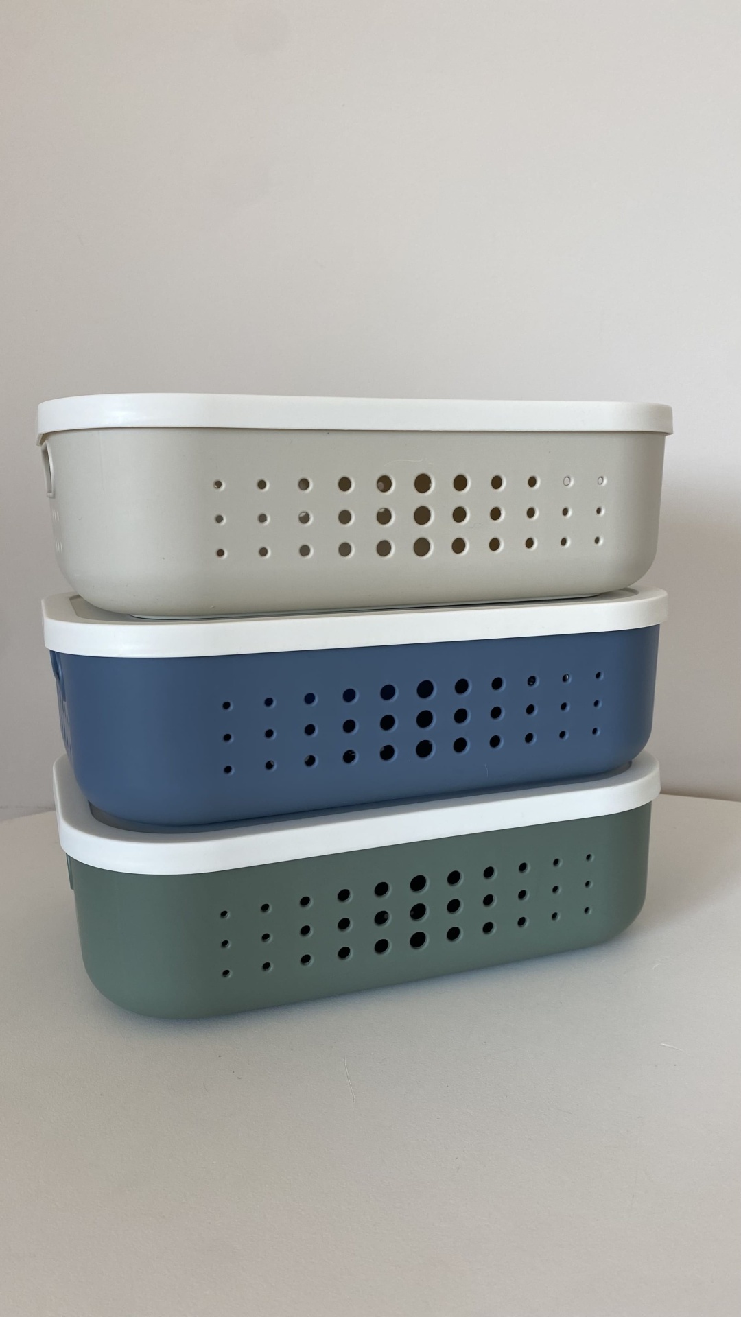 Três caixas de armazenamento plásticas empilhadas com orifícios e tampas brancas.