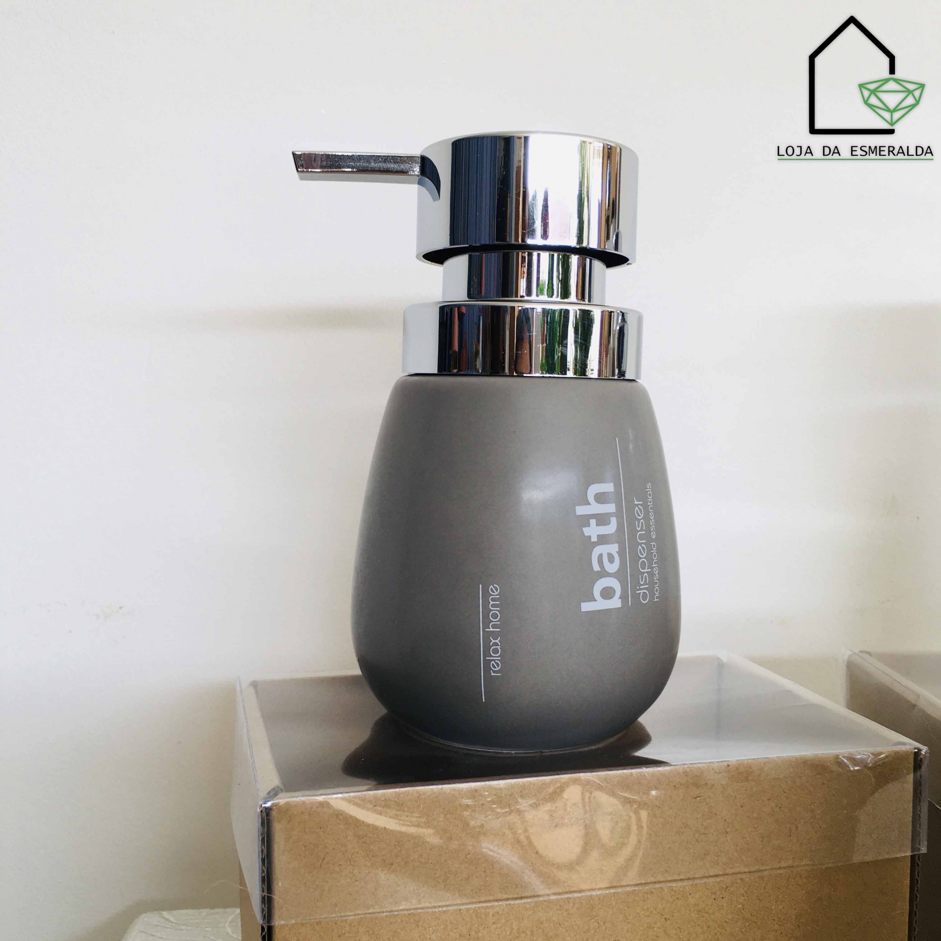 Dispensador de sabão líquido cinza com tampa metálica prateada sobre caixa de cartão