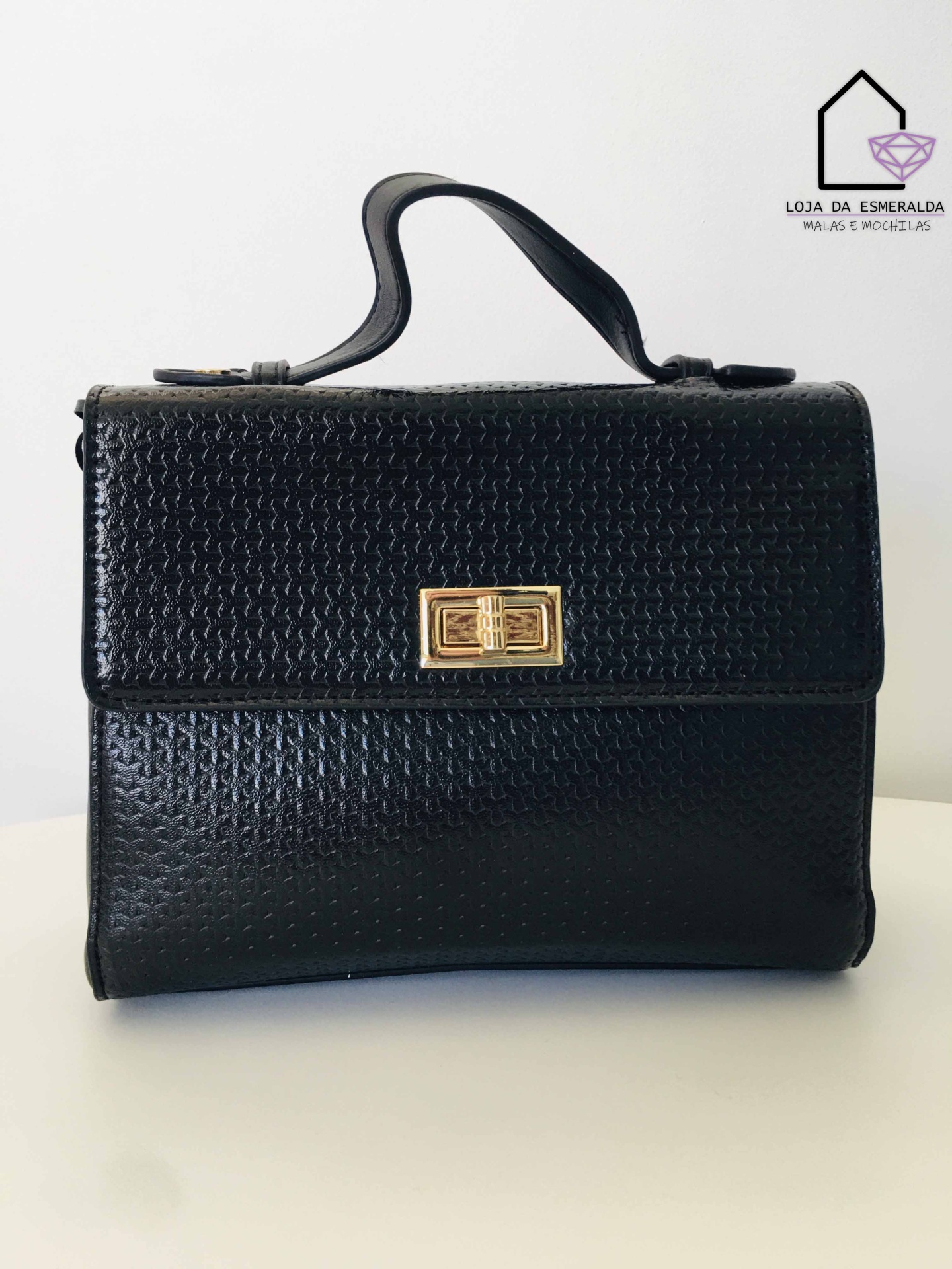 Mala preta em pele com fecho dourado e alça superior sobre fundo branco