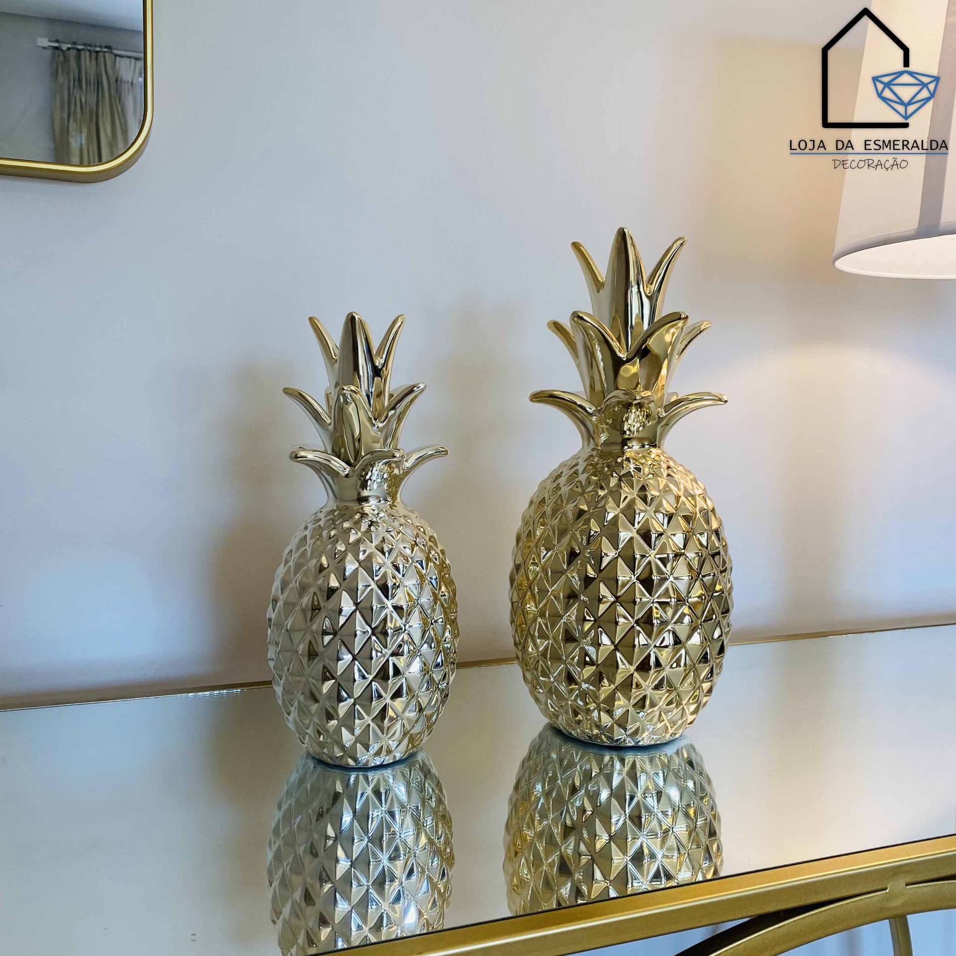 Duas peças decorativas douradas em forma de abacaxi sobre superfície espelhada