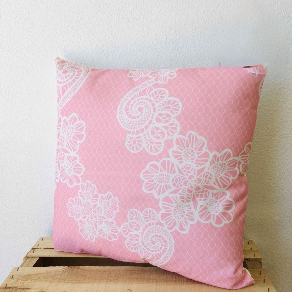 Capa de almofada rosa com padrão branco de flores sobre superfície de madeira clara