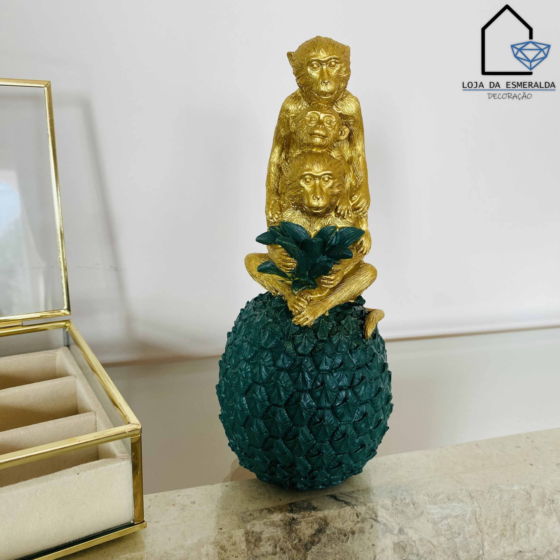 Estatueta decorativa de macacos dourados sobre abacaxi verde escuro com folhas