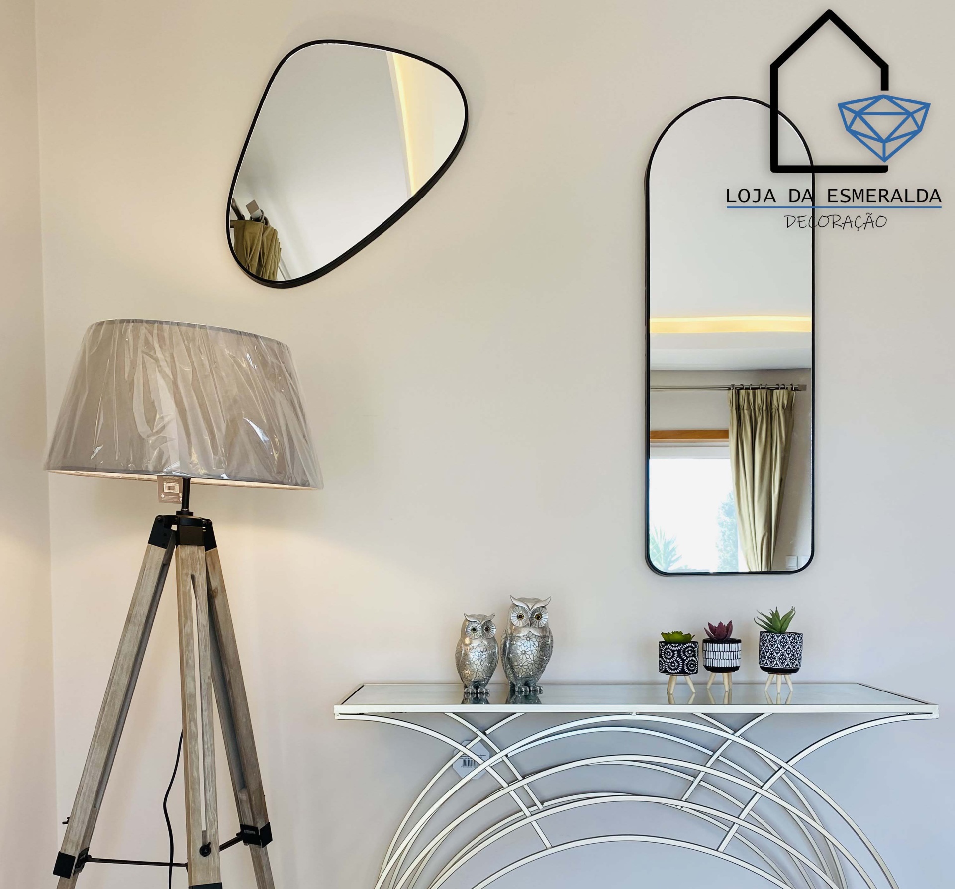 Espaço decorativo com candeeiro, espelhos, consola e decoração com corujas e vasos.