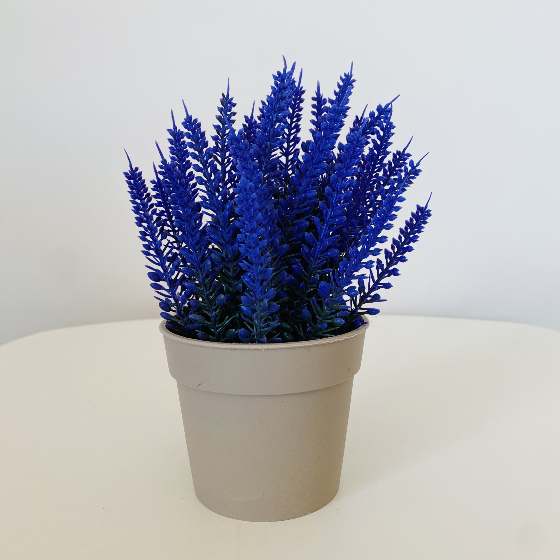 Vaso bege com plantas artificiais azuis sobre mesa branca