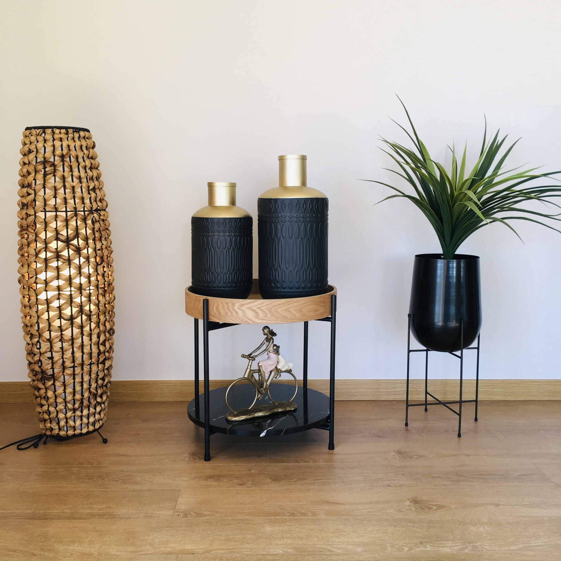 Decoração com lâmpada trançada, mesa com garrafas e estatueta e vaso com planta num piso de madeira