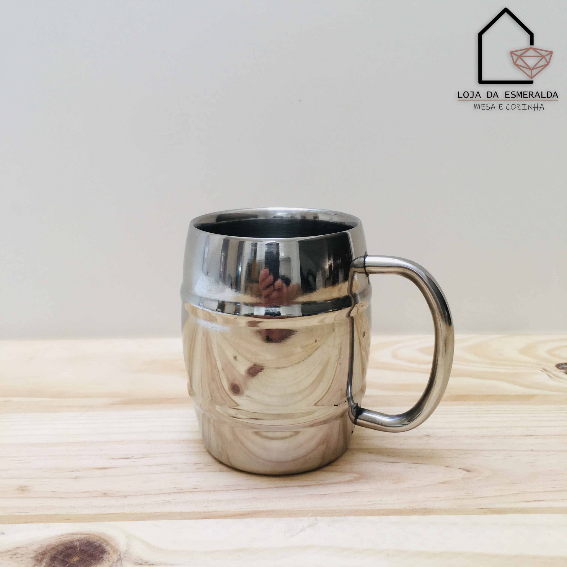 Caneca metálica brilhante sobre mesa de madeira com logotipo ao fundo