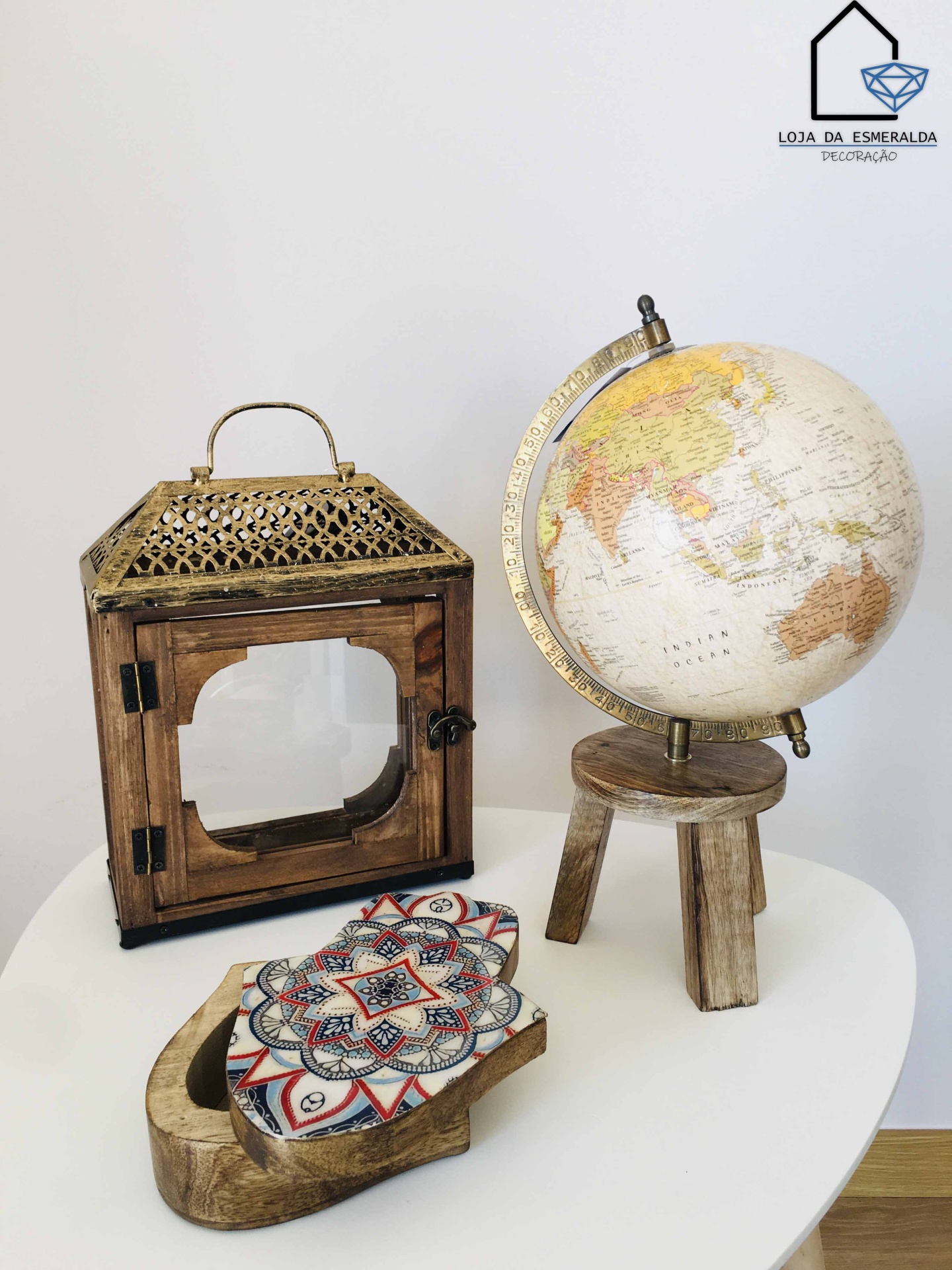 Globo terrestre, candeeiro de madeira com detalhes dourados e base de madeira com azulejos geométricos numa mesa branca