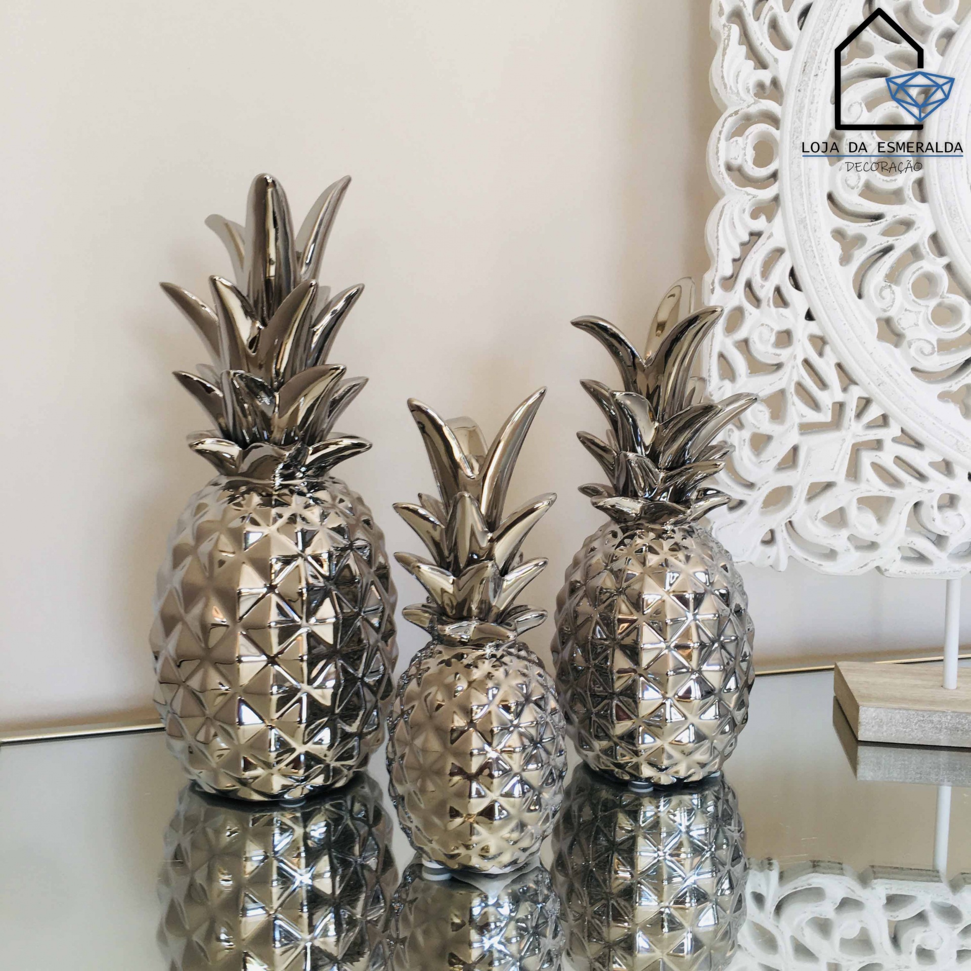Três abacaxis metálicos decorativos prateados sobre superfície espelhada