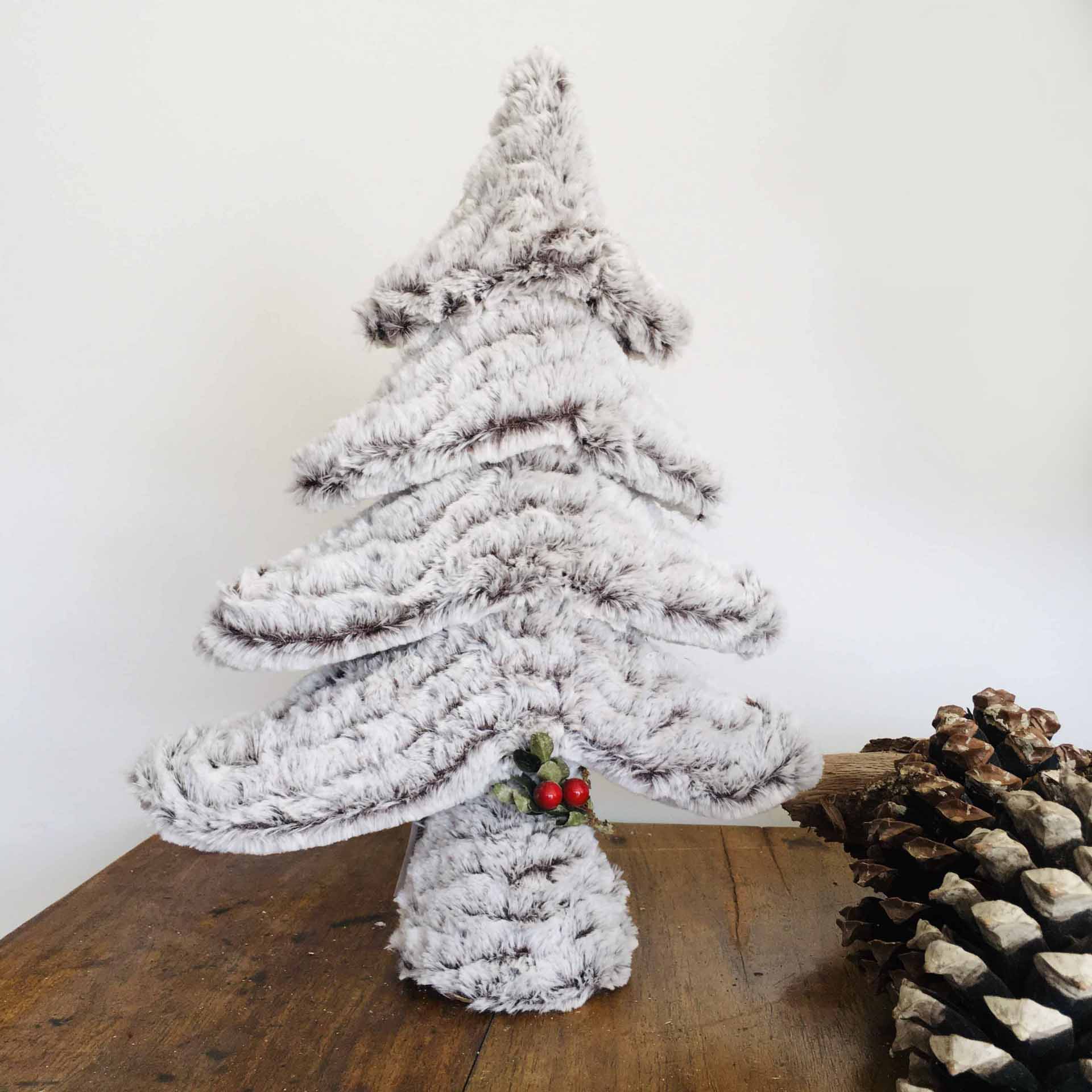 Árvore de Natal de pelúcia branca com decoração vermelha e verde sobre mesa de madeira