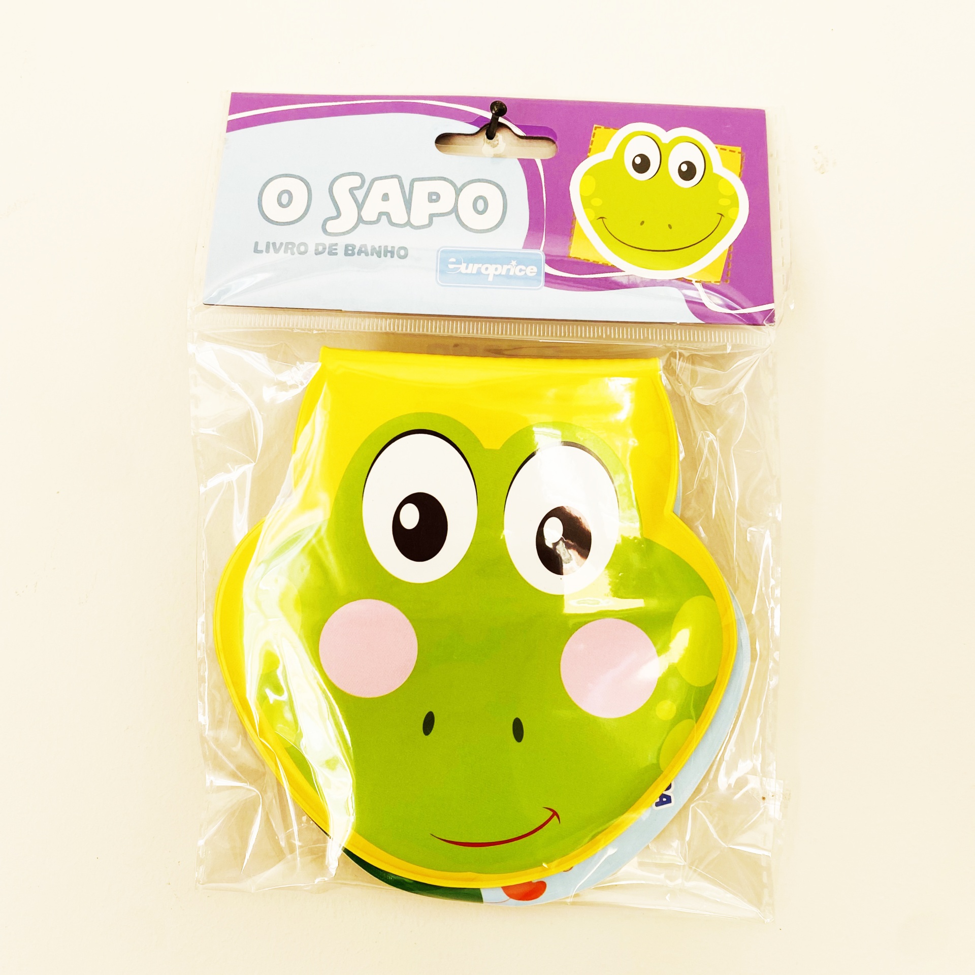 Livro de banho em forma de sapo verde com bochechas cor de rosa embalada em plástico.