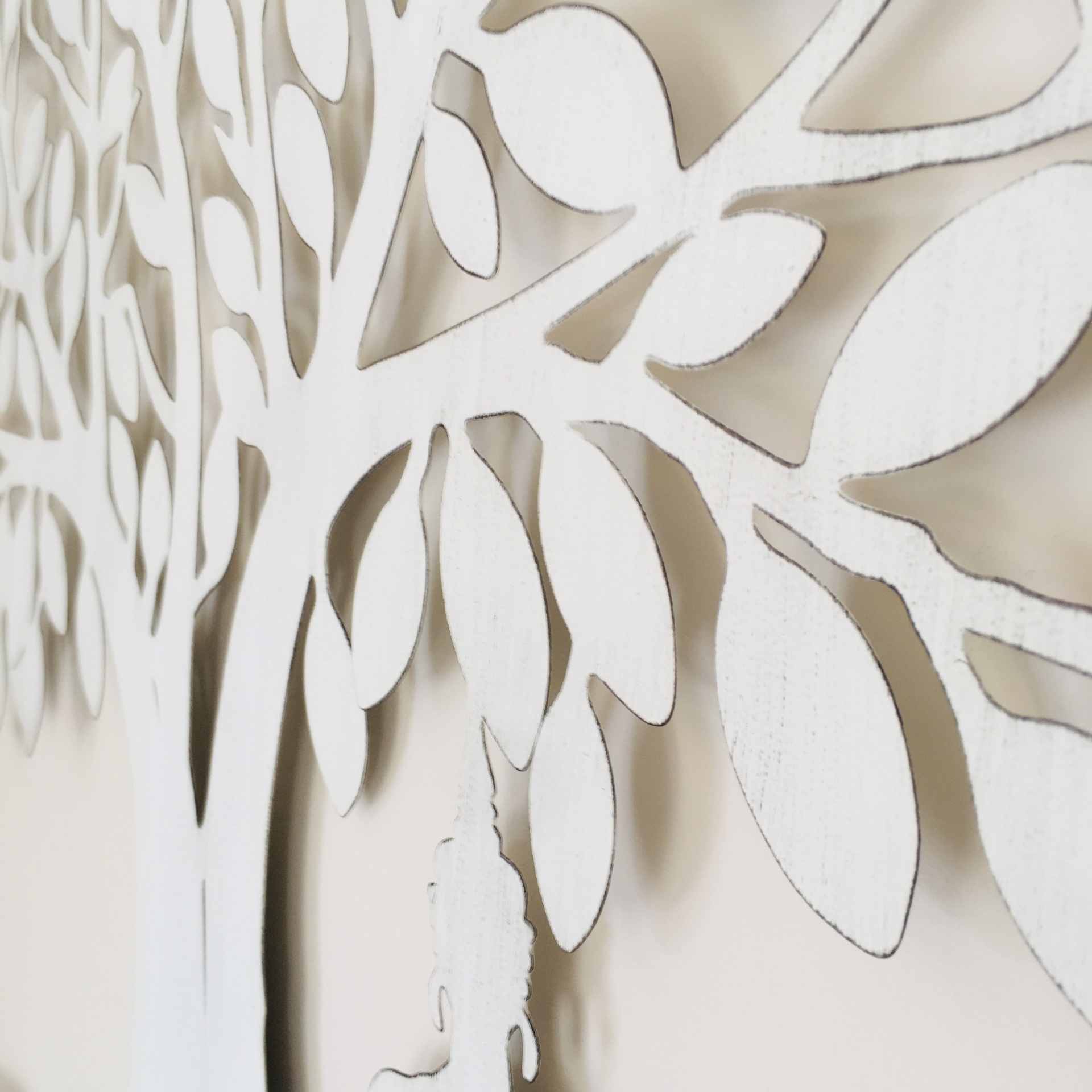 Painel decorativo de madeira branca com desenho de árvore e folhas recortadas