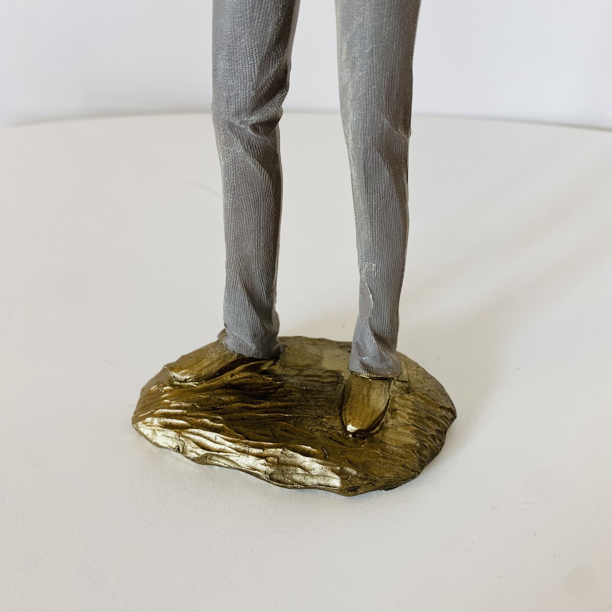 Figura decorativa com calças cinzentas e sapatos dourados numa base dourada