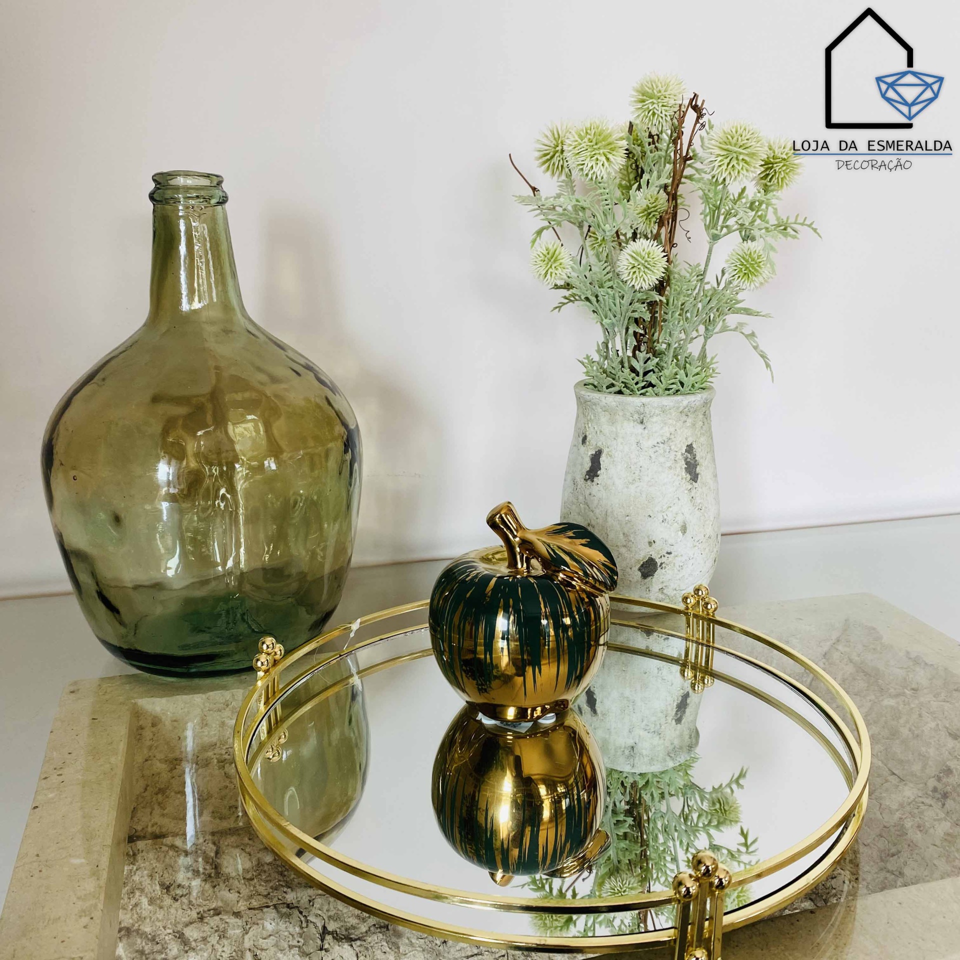 Conjunto decorativo com vaso de vidro verde, vaso branco com flores e tabuleiro espelhado redondo com abóbora dourada