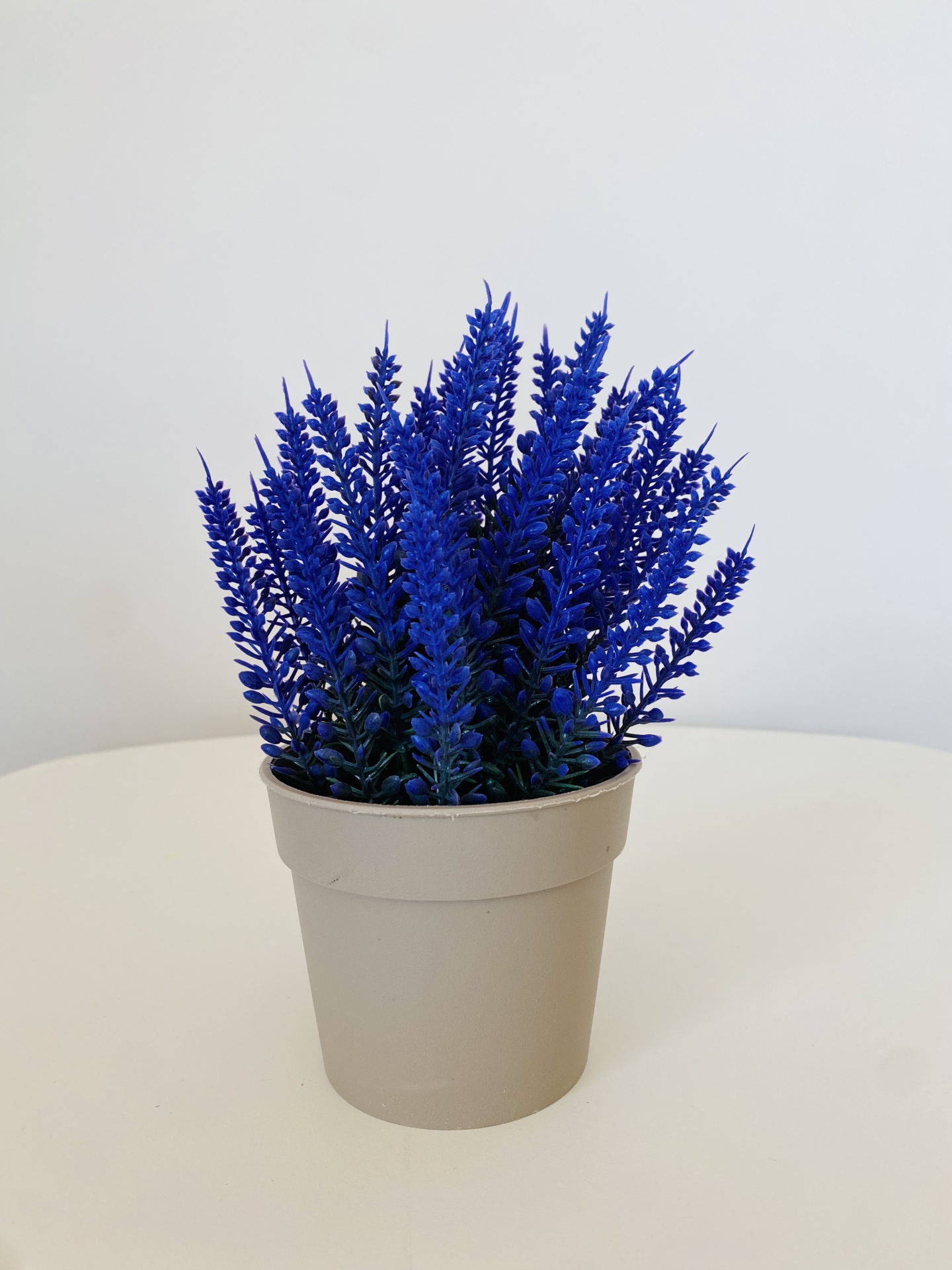 Vaso cinzento com planta artificial azul sobre mesa branca