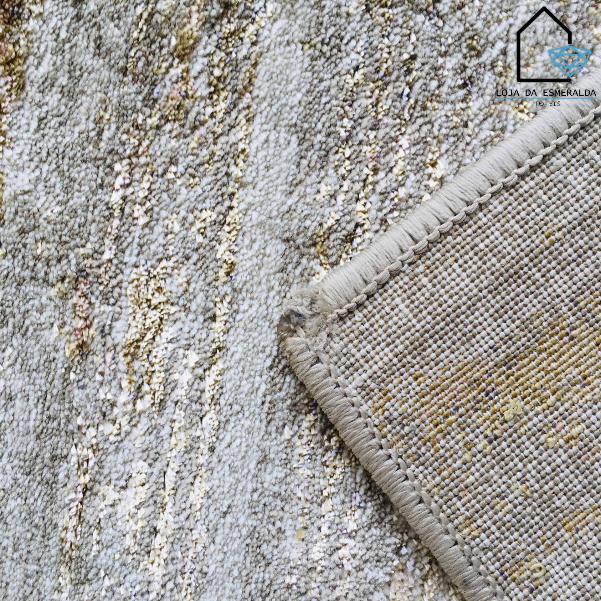 Detalhe de tapete cinzento com padrões em tons bege e castanho claro e borda costurada