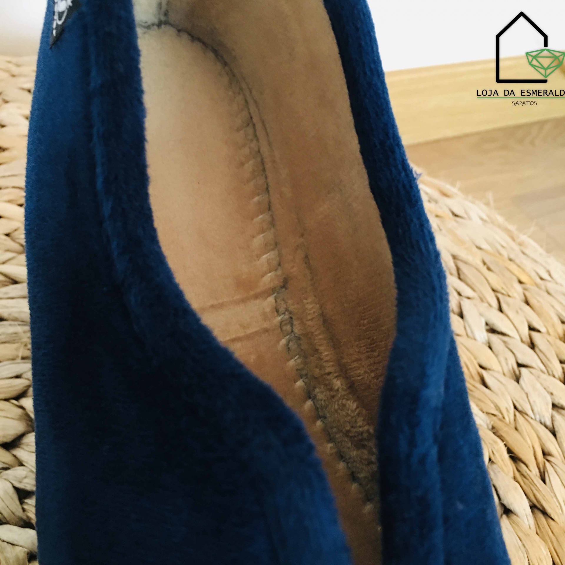 Sapato azul escuro aveludado com interior castanho claro sobre superfície de palha trançada