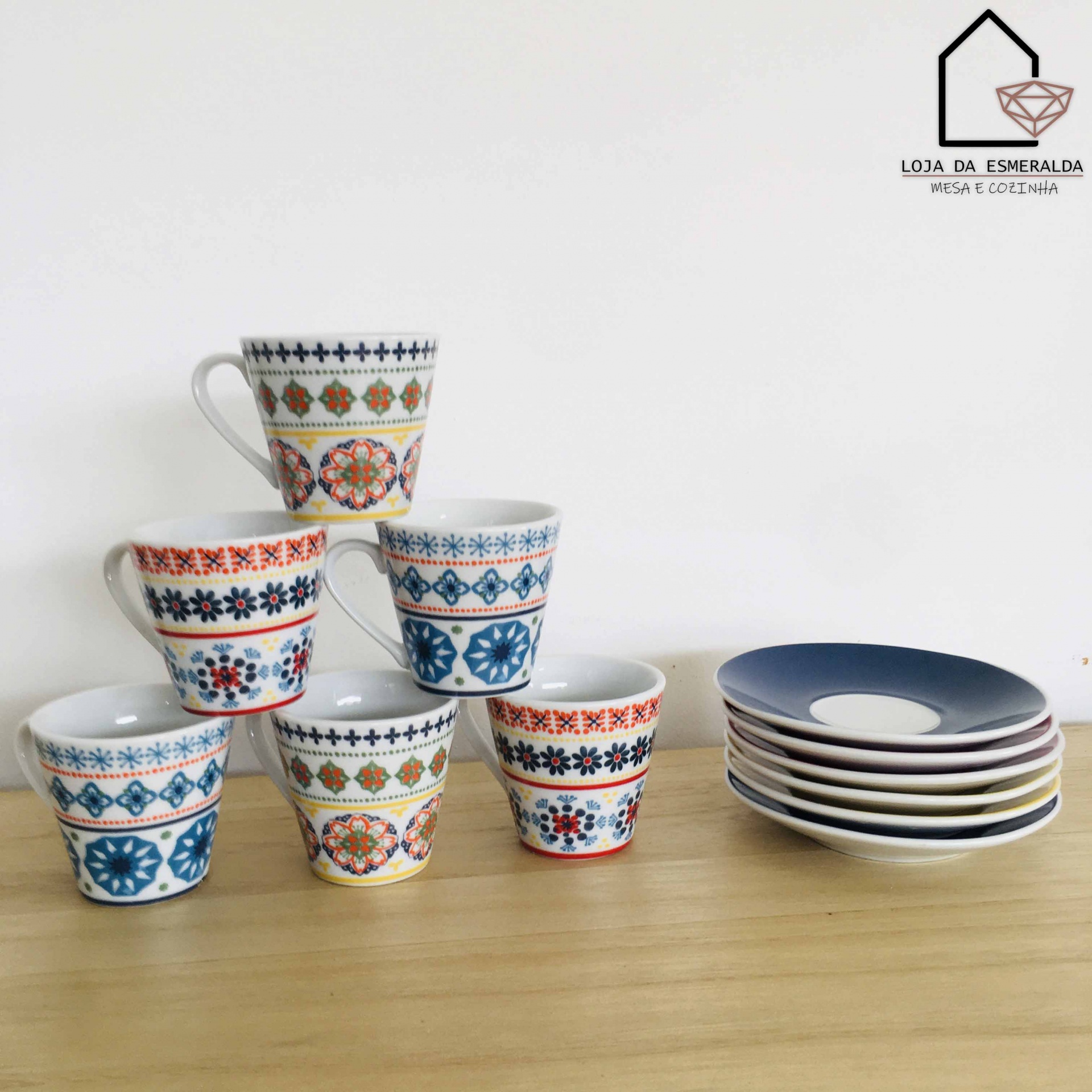 Conjunto de chávenas em cerâmica com padrões coloridos e pequenas chávenas azuis sobre mesa de madeira