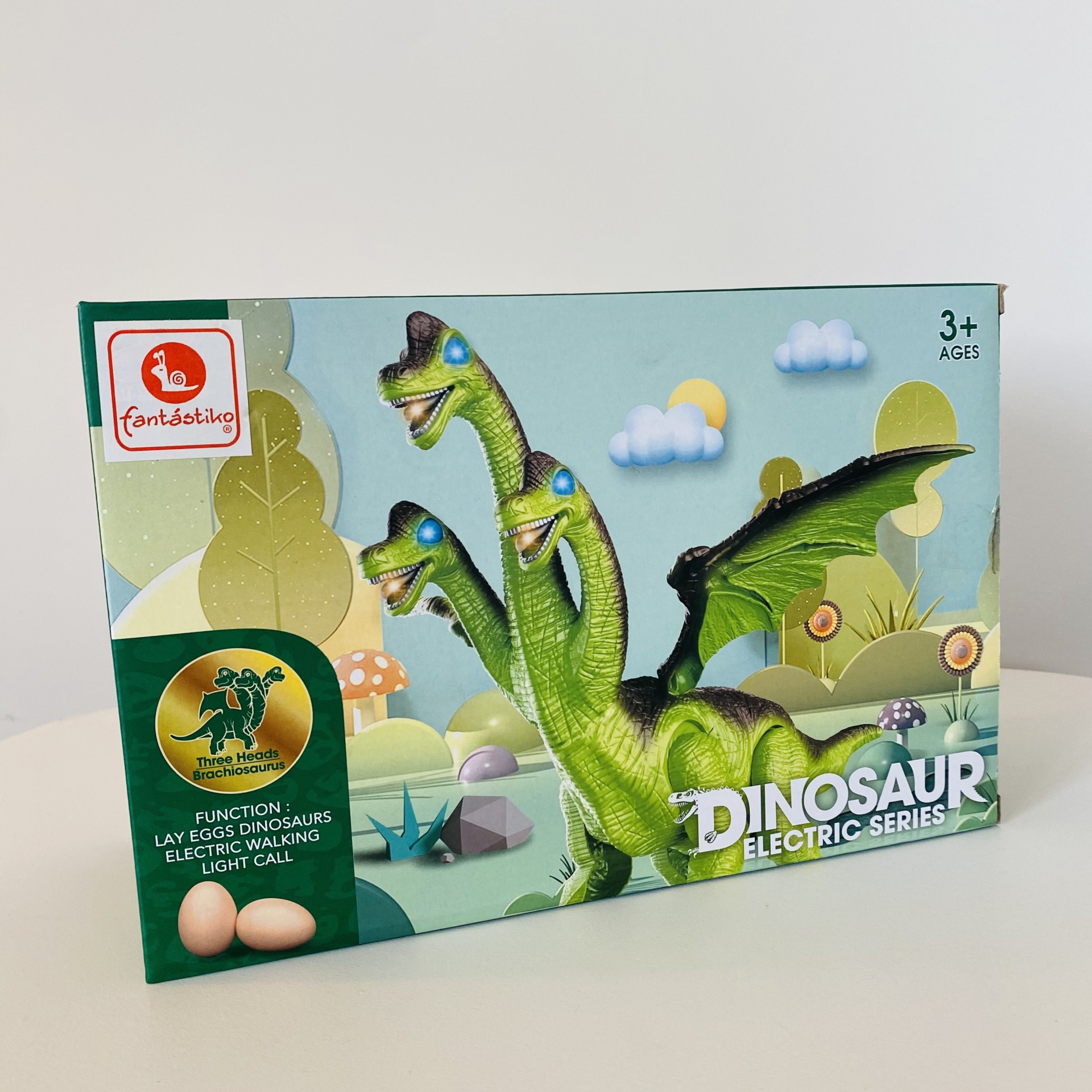 Caixa com brinquedo de dinossauro verde de três cabeças e asas para crianças, texto com funções e idade recomendada