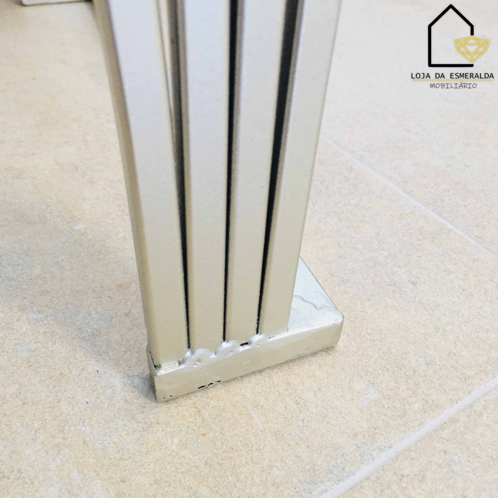 Pé metálico de móvel desgastado sobre chão de azulejos claros e logótipo da loja