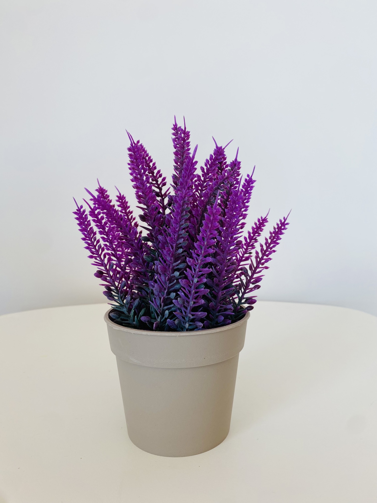 Planta artificial púrpura em vaso cinza claro sobre superfície branca