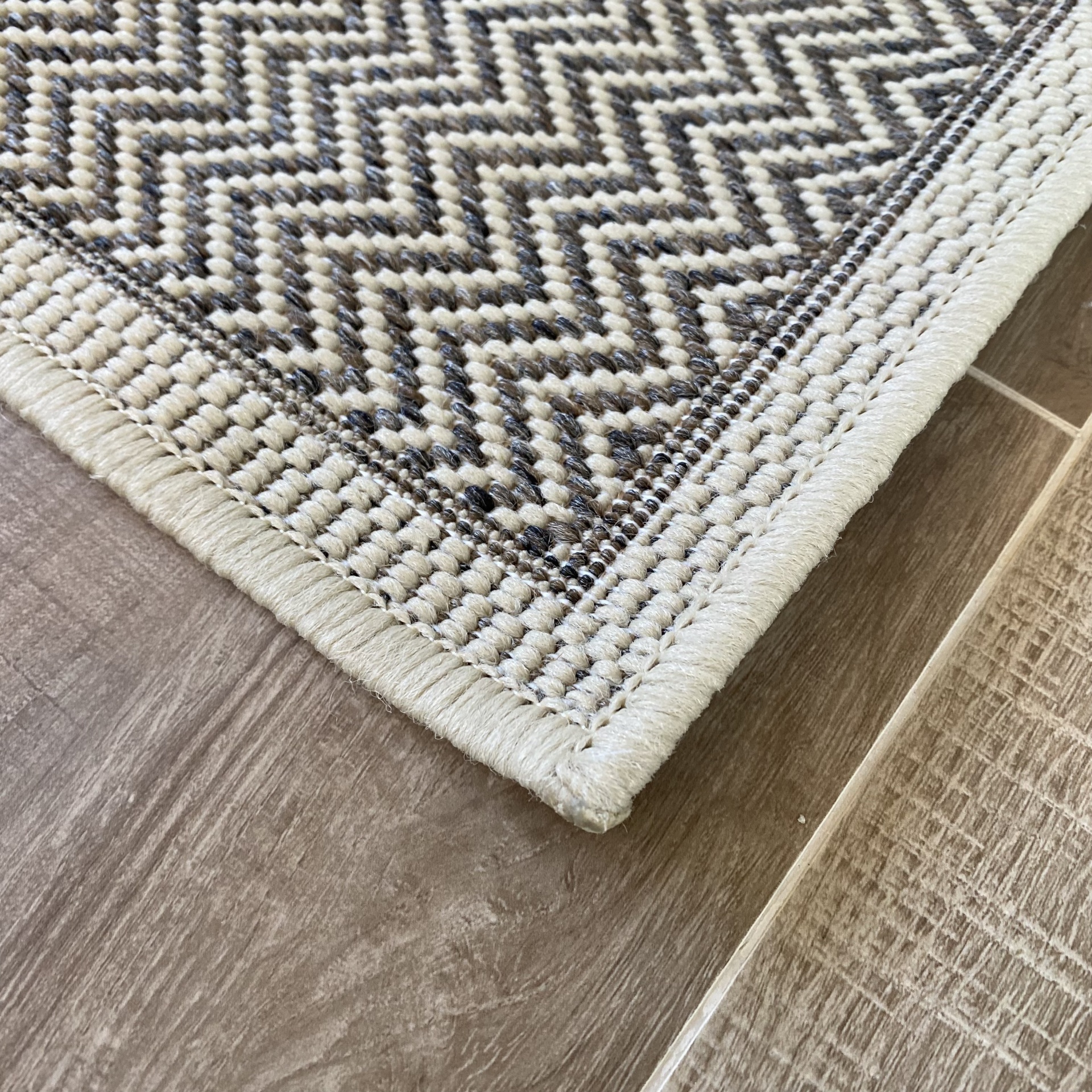 Pormenor de tapete de tecido com padrão em zig-zag bege e castanho sobre chão de azulejos castanho claro