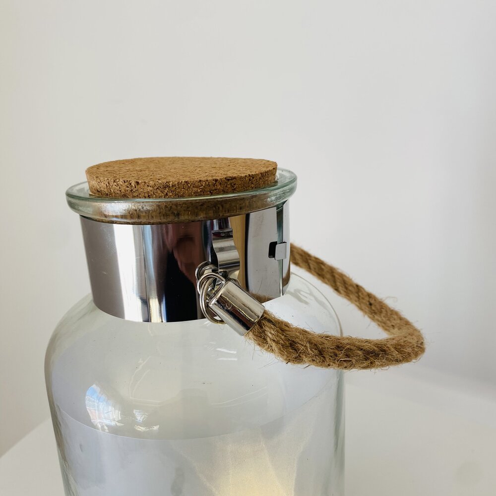 Garrafa de vidro com tampa de cortiça, borda metálica e alça de corda.