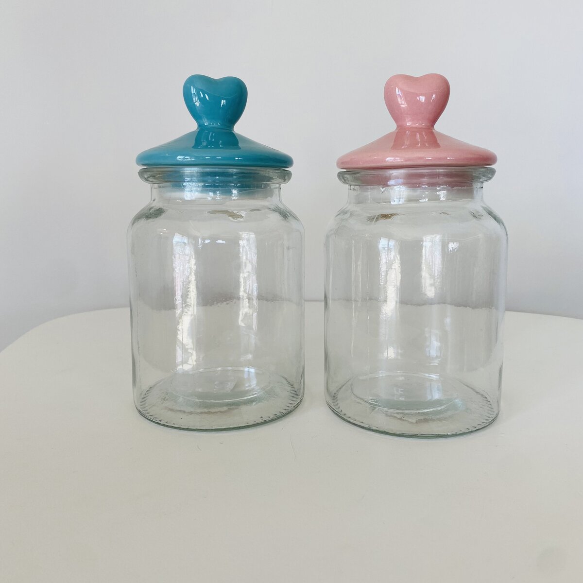 Dois frascos de vidro com tampas de cerâmica azul e rosa em forma de coração