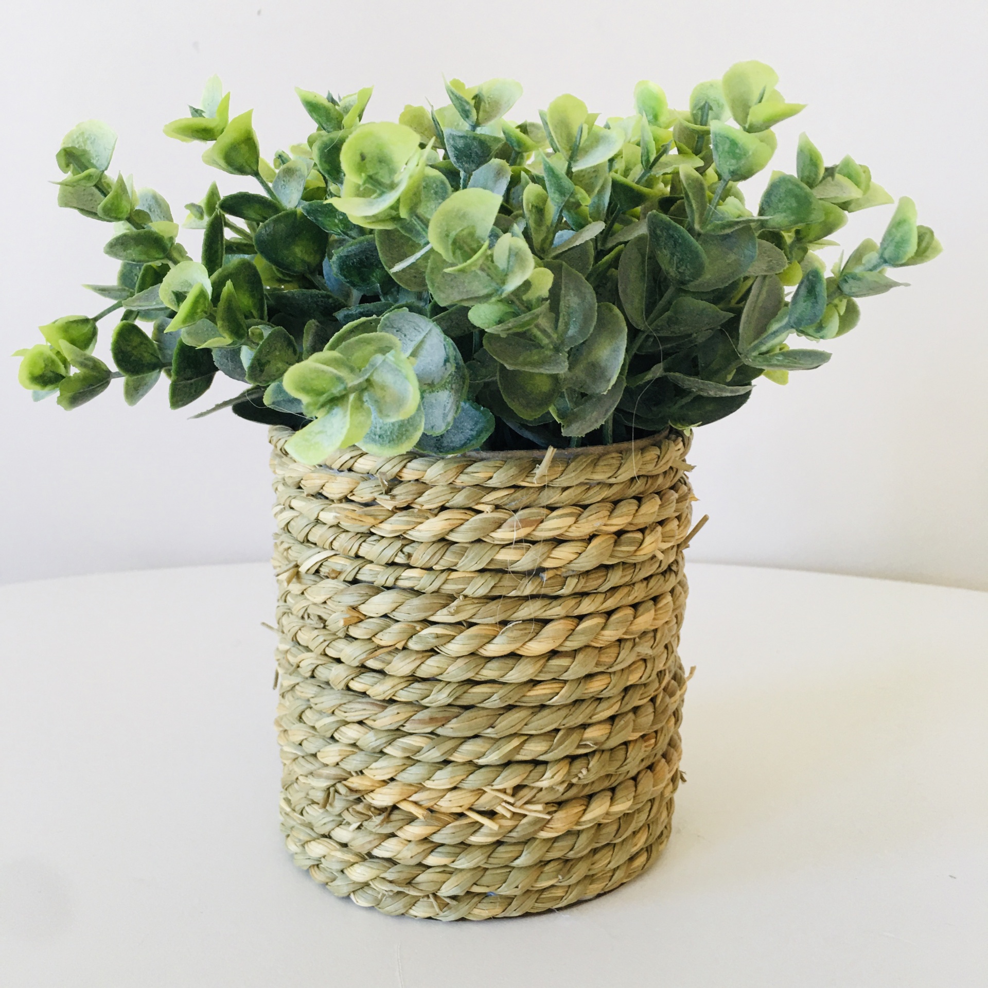 Vaso redondo trançado com plantas artificiais verdes sobre superfície branca