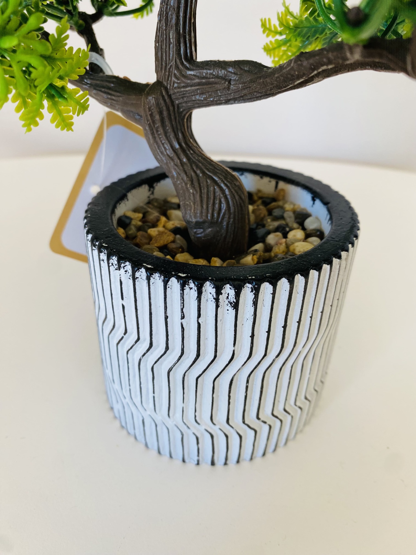 Vaso decorativo branco com padrão geométrico preto e tronco artificial castanho com pedras na base