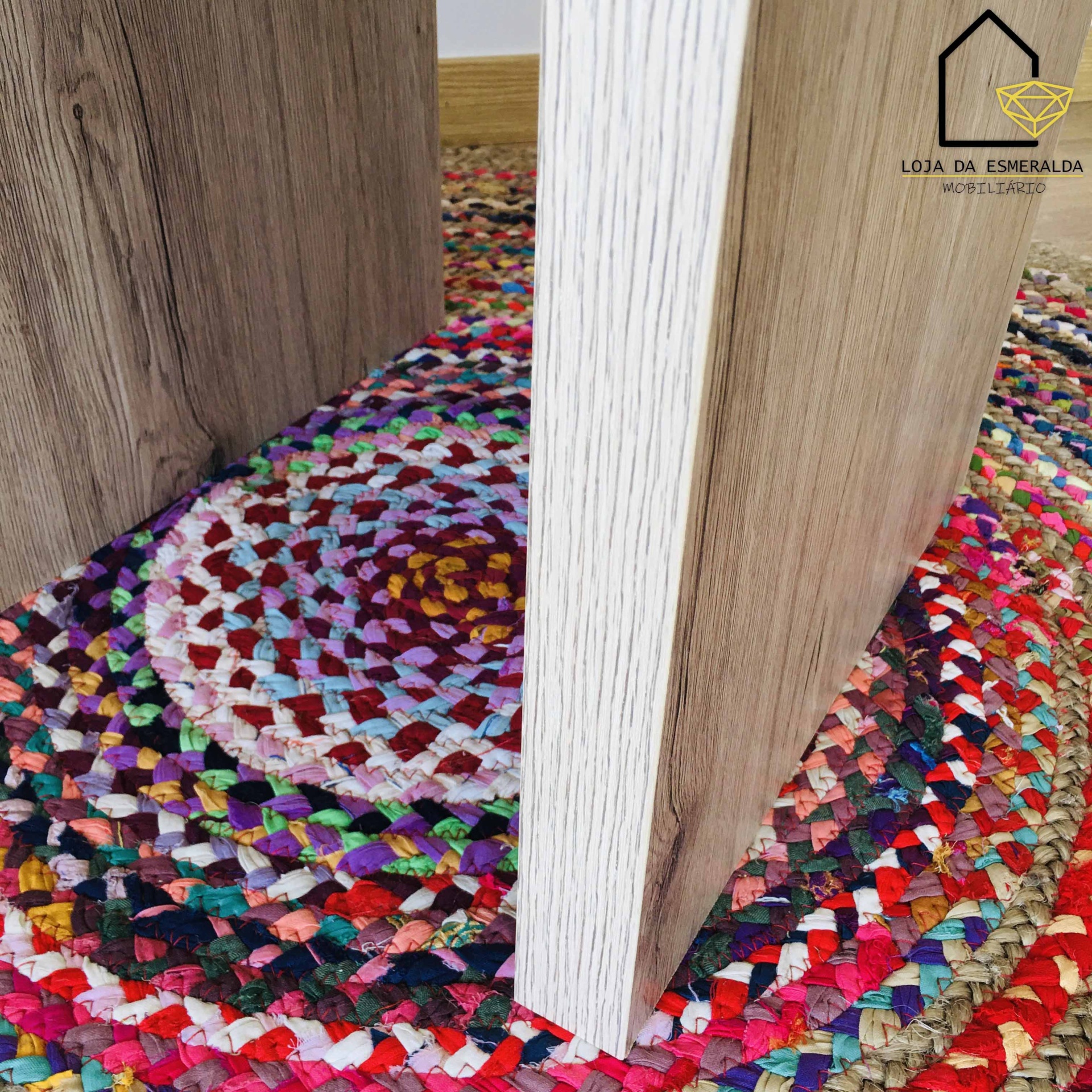 Peças de mobiliário em madeira clara sobre tapete redondo colorido no chão de madeira.