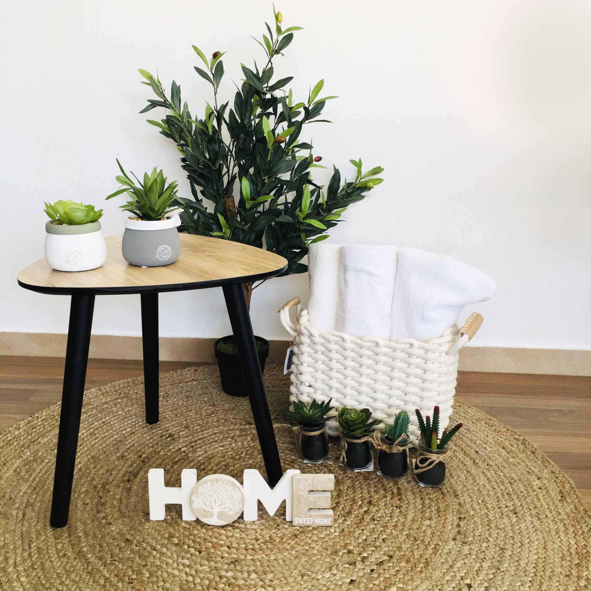 Mesa redonda de madeira e preto com plantas e cesta branca com toalhas sobre tapete redondo de fibra