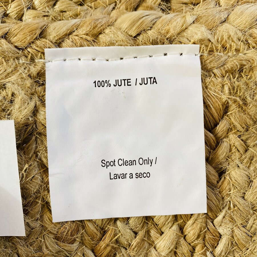 Etiqueta de juta com informações de material e cuidados, sobre superfície de juta trançada.