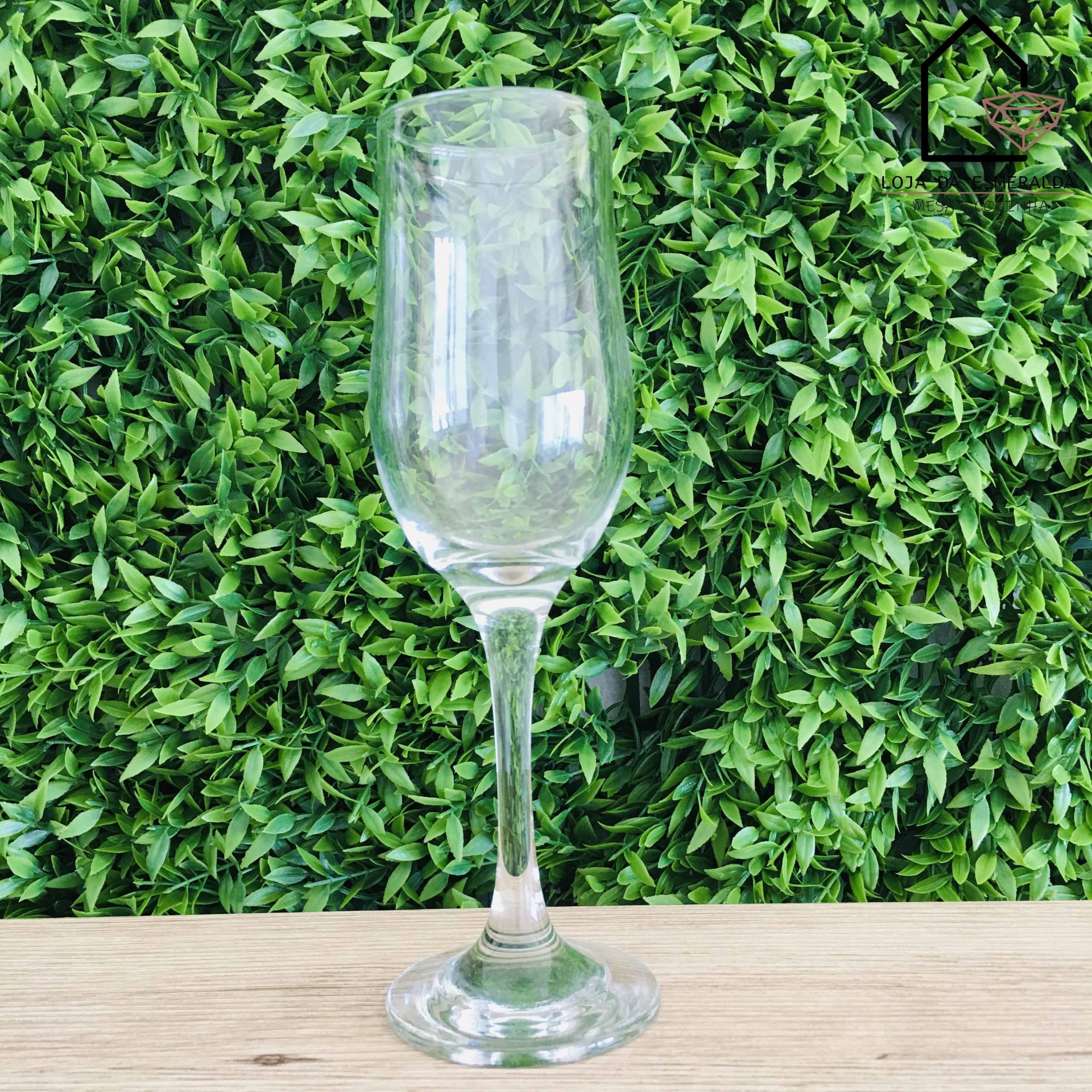 Copo de vidro tipo flute sobre superfície de madeira com fundo de folhas verdes