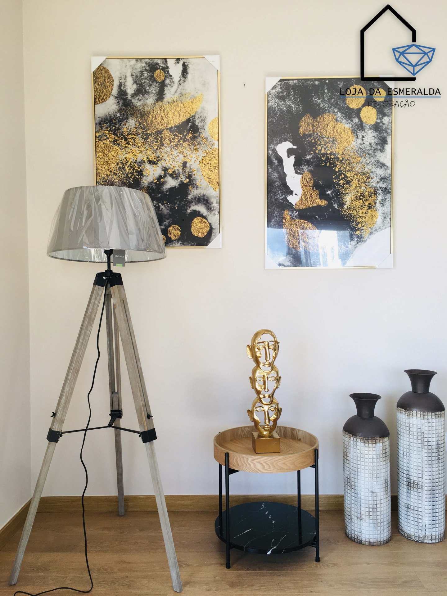 Decoração interior com abajur de tripé, mesa redonda, escultura dourada, jarros texturizados e quadros abstratos