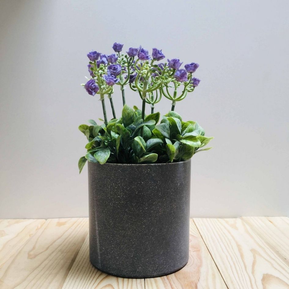 Vaso cinza com planta artificial de folhas verdes e flores roxas