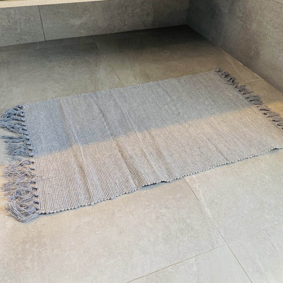 Tapete cinzento claro com franjas, em piso de azulejos cinzentos