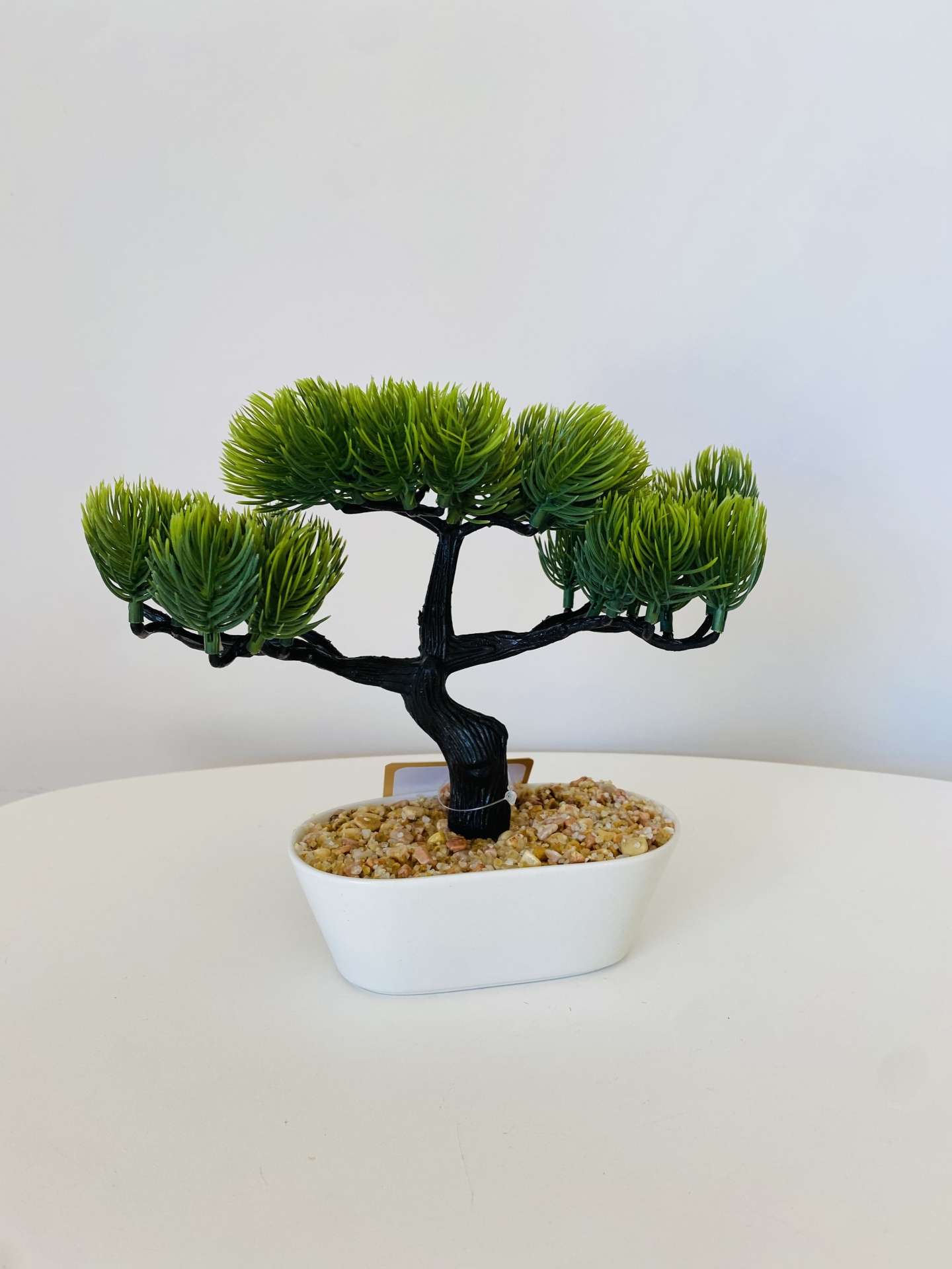 Árvore artificial decorativa com folhas verdes e base branca com pedras.