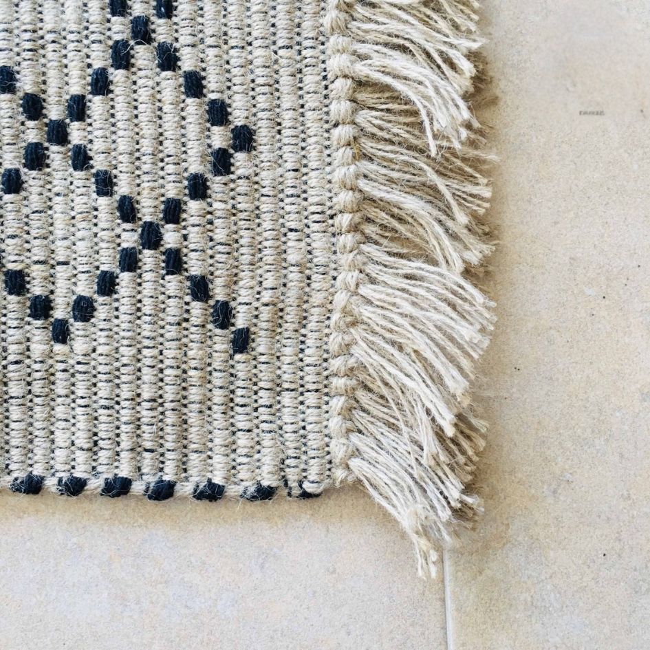 Tapete tecido bege com padrão preto e franjas em chão claro